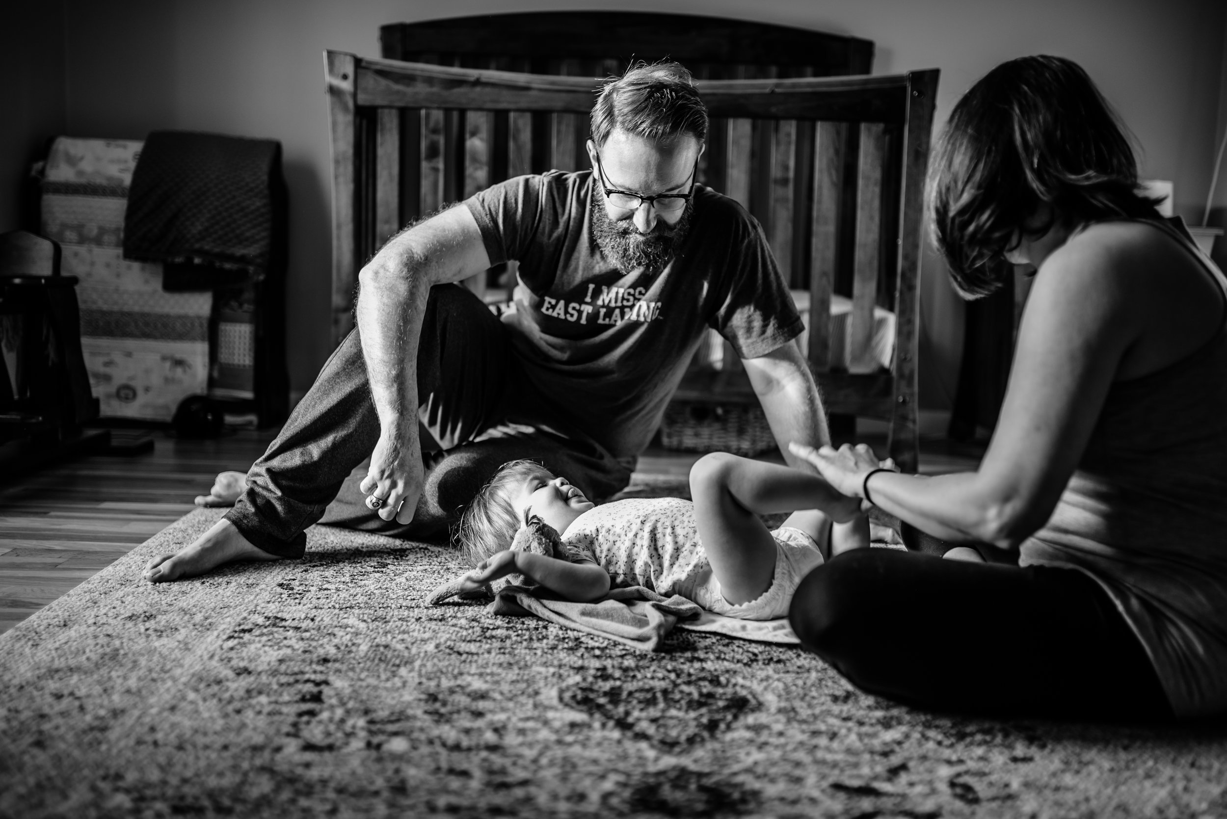 Mom and Dad change daughter's diaper on rug