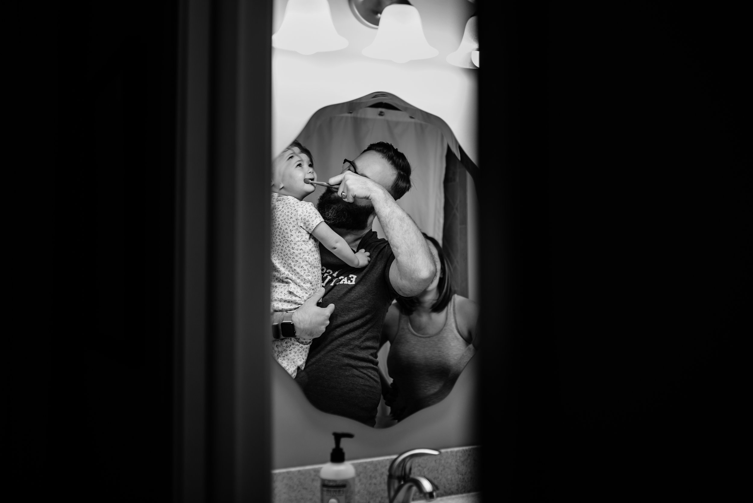 Reflection in mirror of Dad brushing daughter's teeth