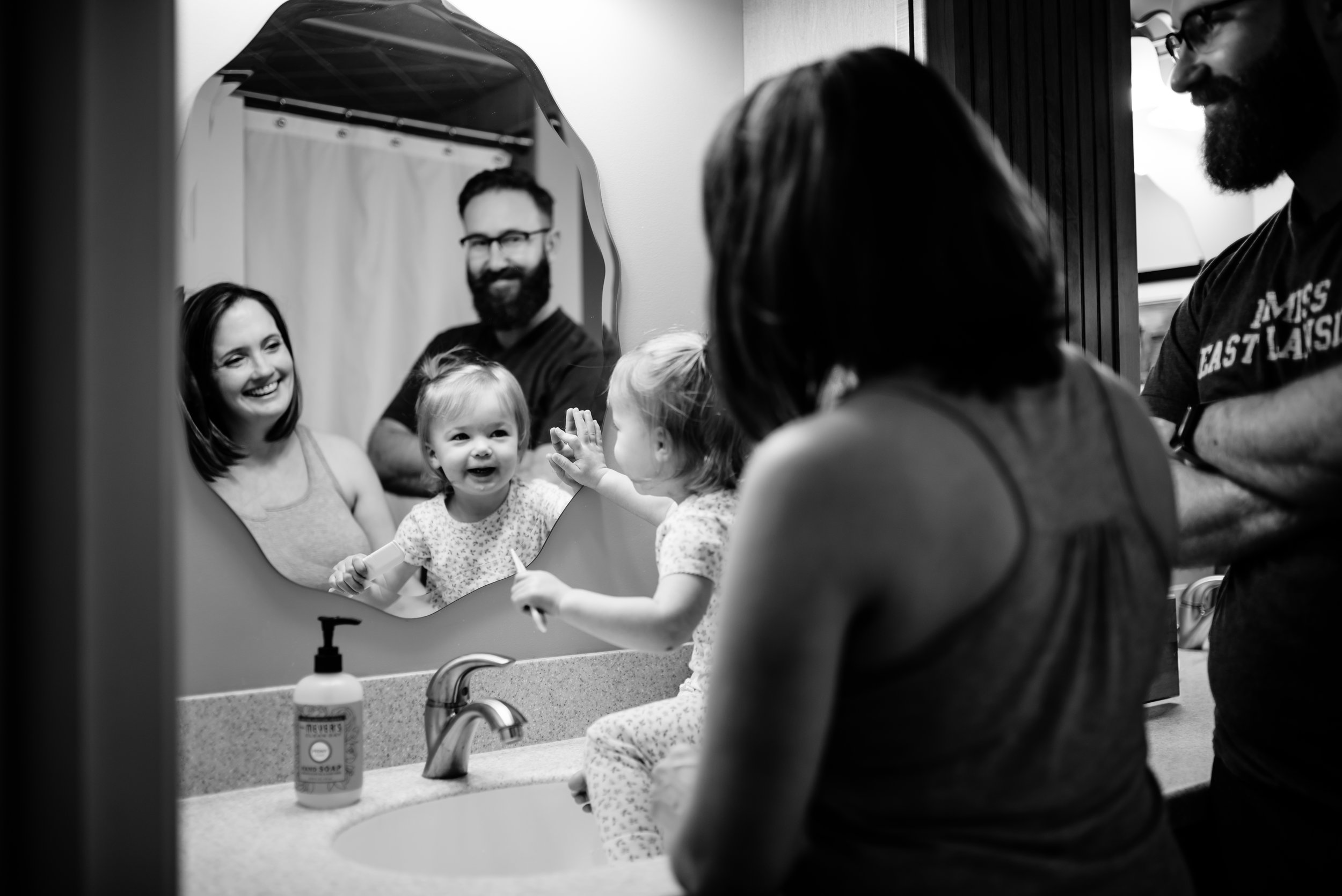 Parents and daughter smile at their reflection in bathroom mirror