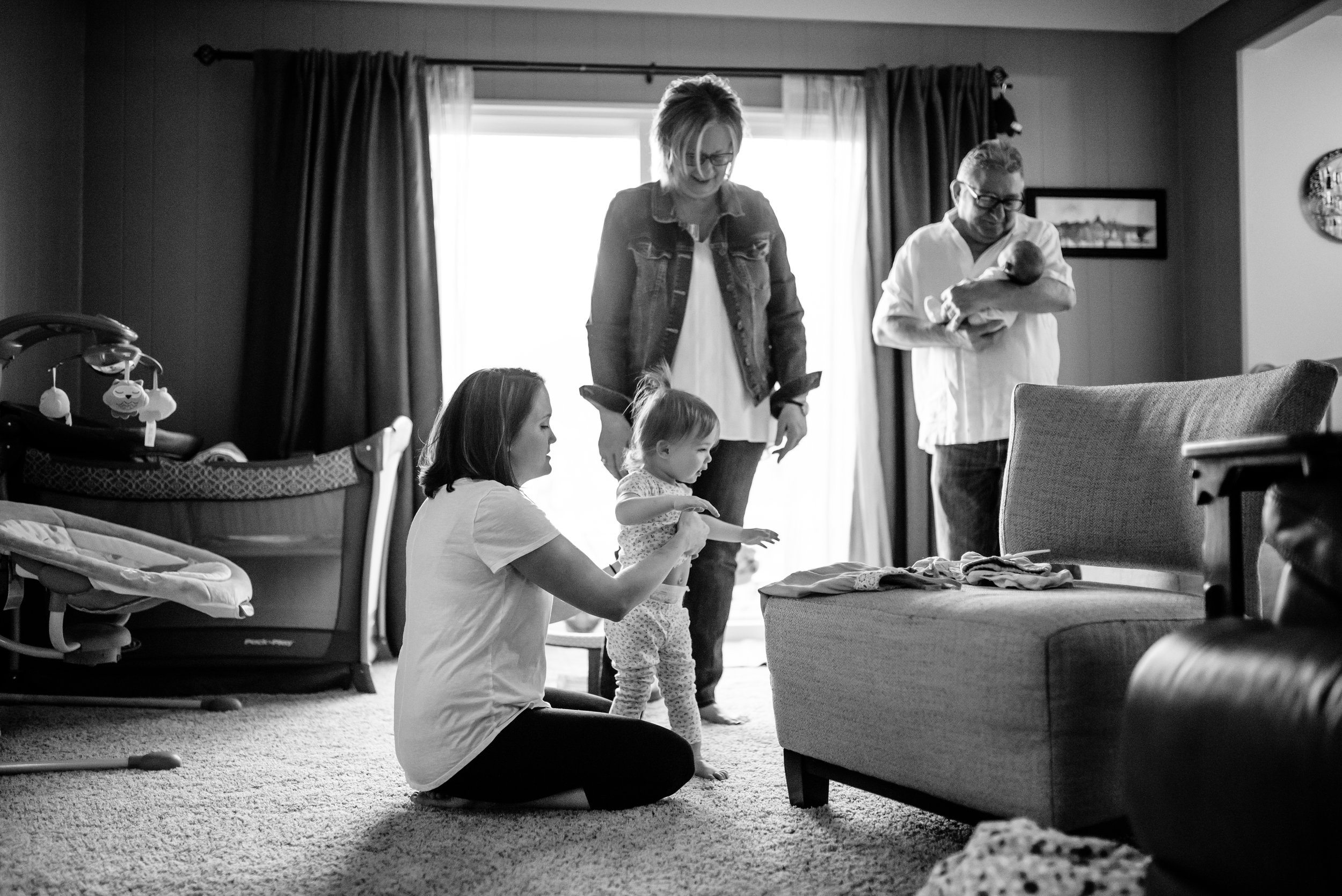 Mom starts to get toddler dressed while grandparents watch and hold baby