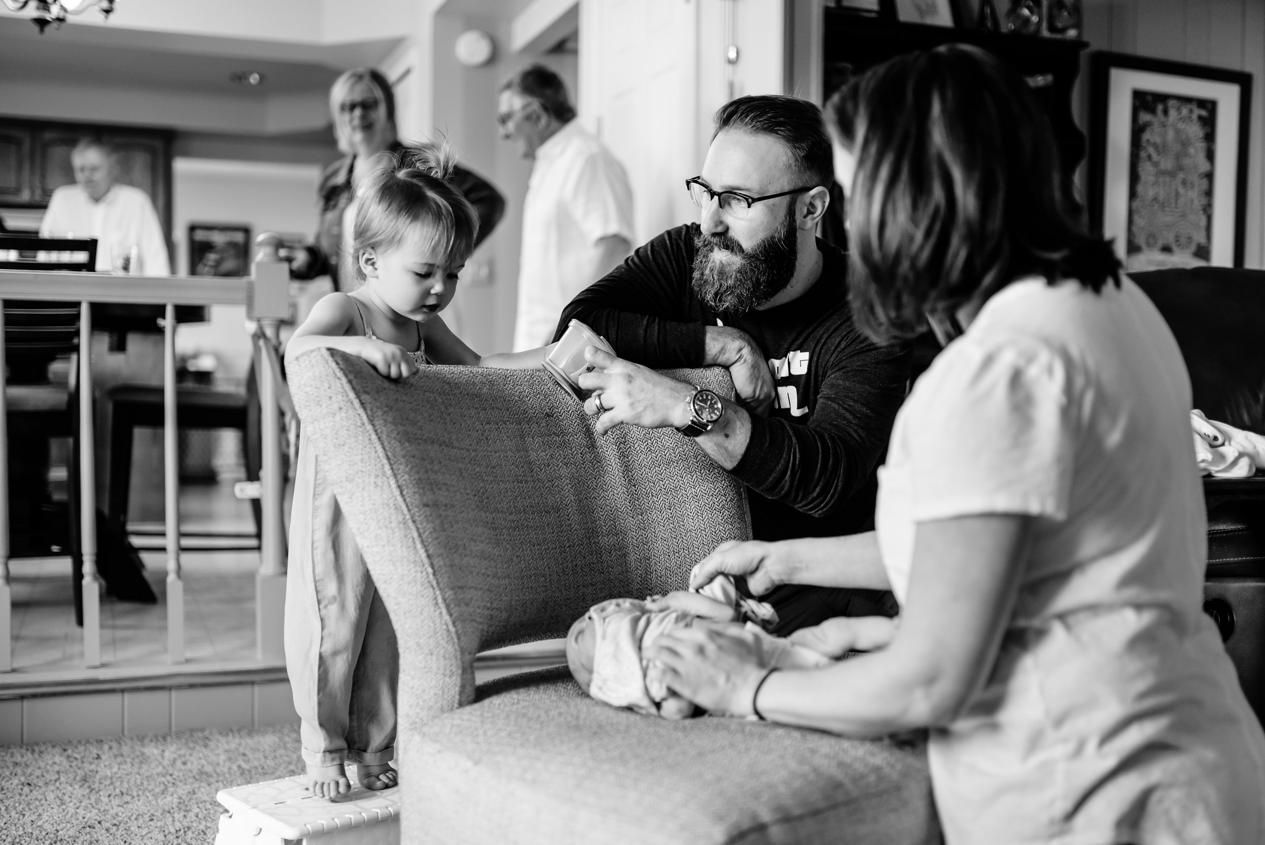 Girl looks at baby sister being dressed on chair