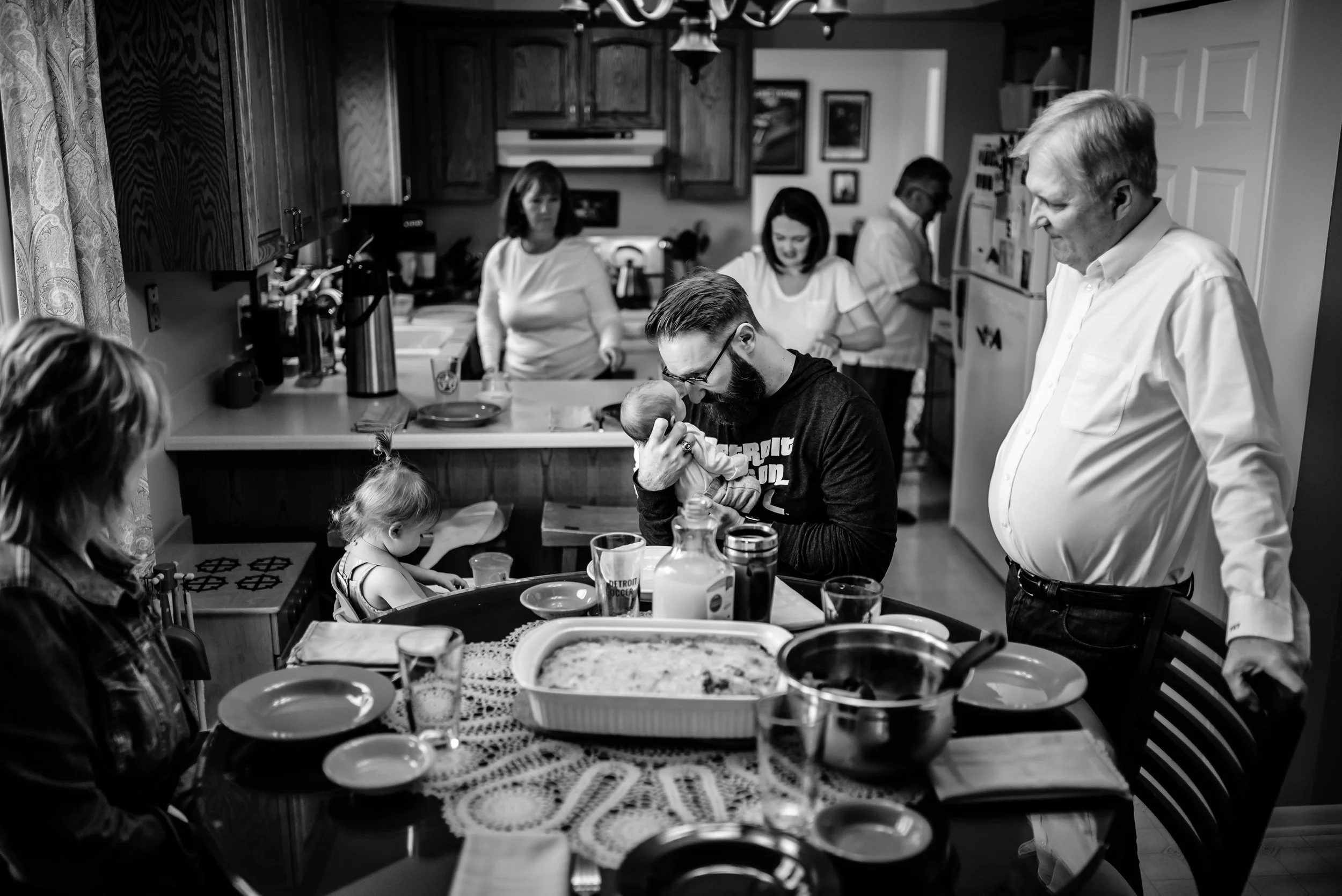 Family gathers for meal in kitchen, Dad has special moment with baby in center of chaos