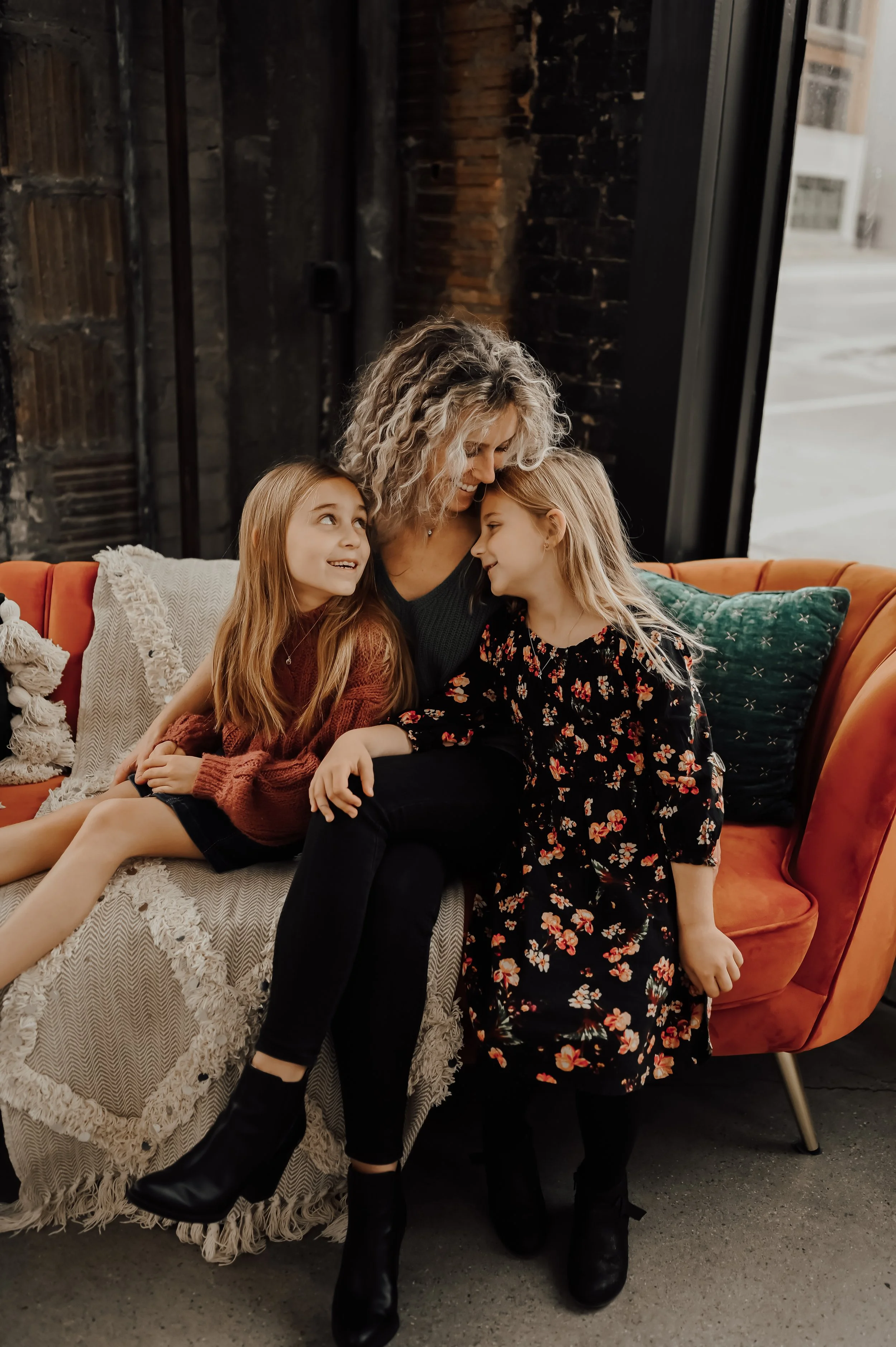 mom and daughters smiling and snuggling on couch