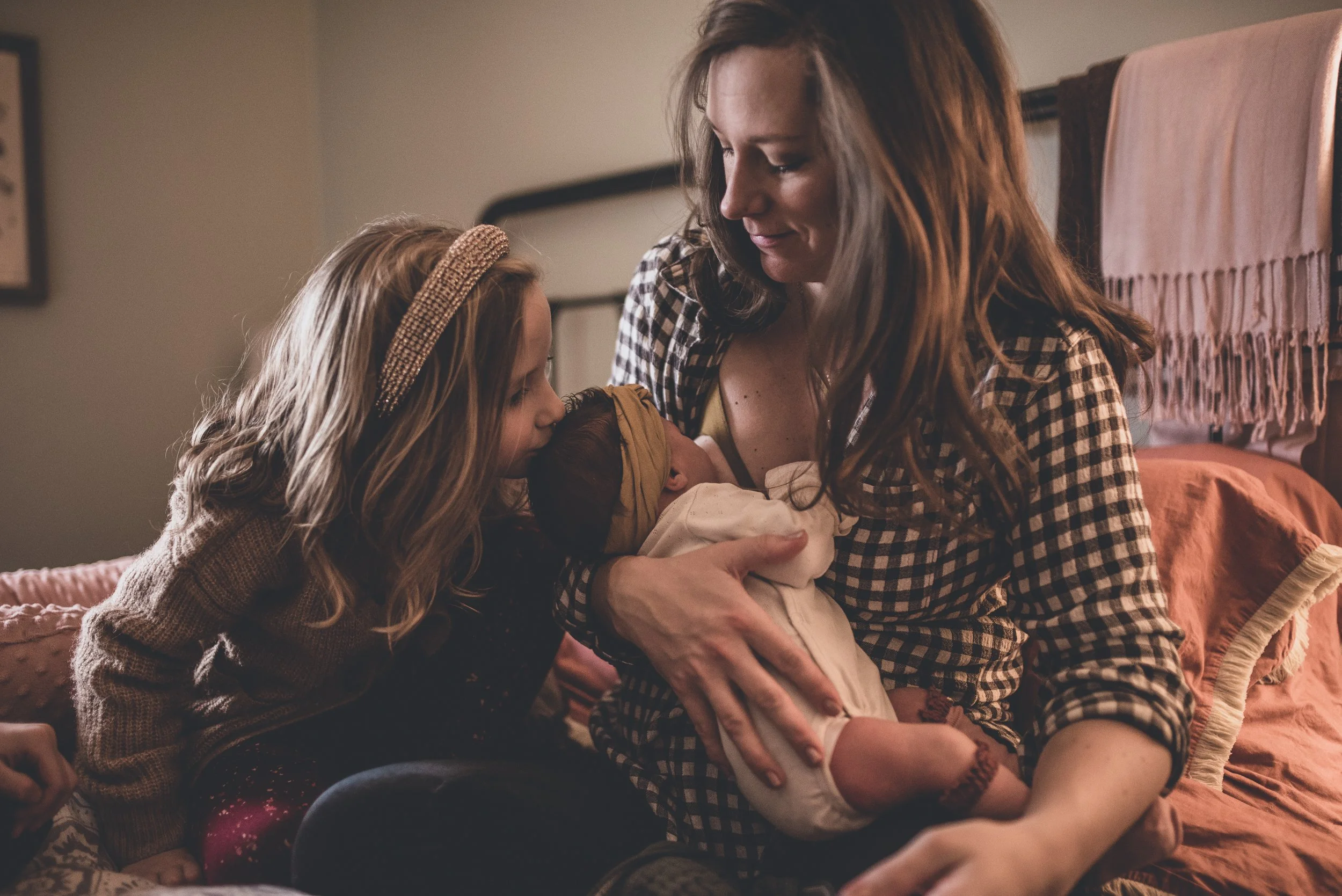 big sister kisses baby while mom is nursing baby