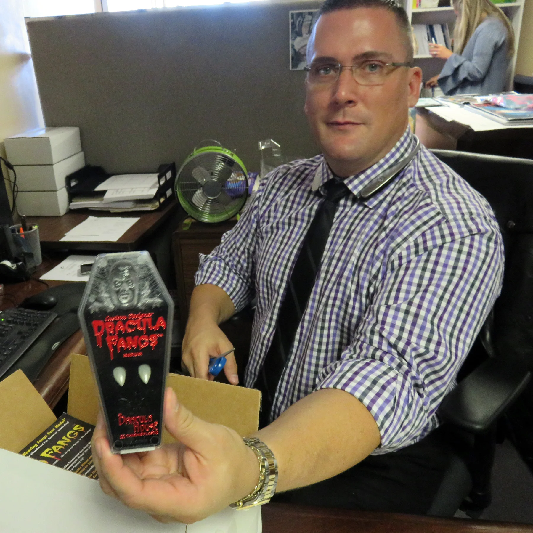 Jason Cobb, Office and Educational Outreach Manager, showing off a package of Dracula fangs.)