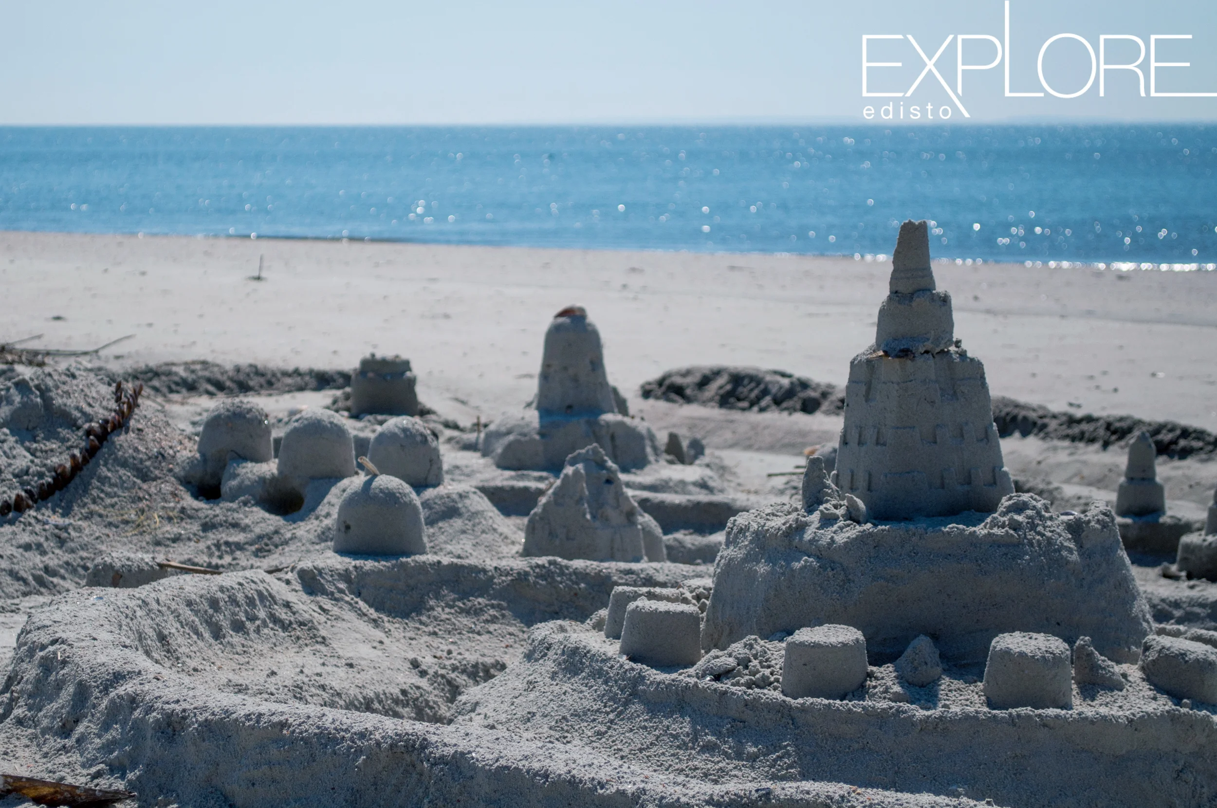 Sand castle on the beach with ocean sparkling in the background.