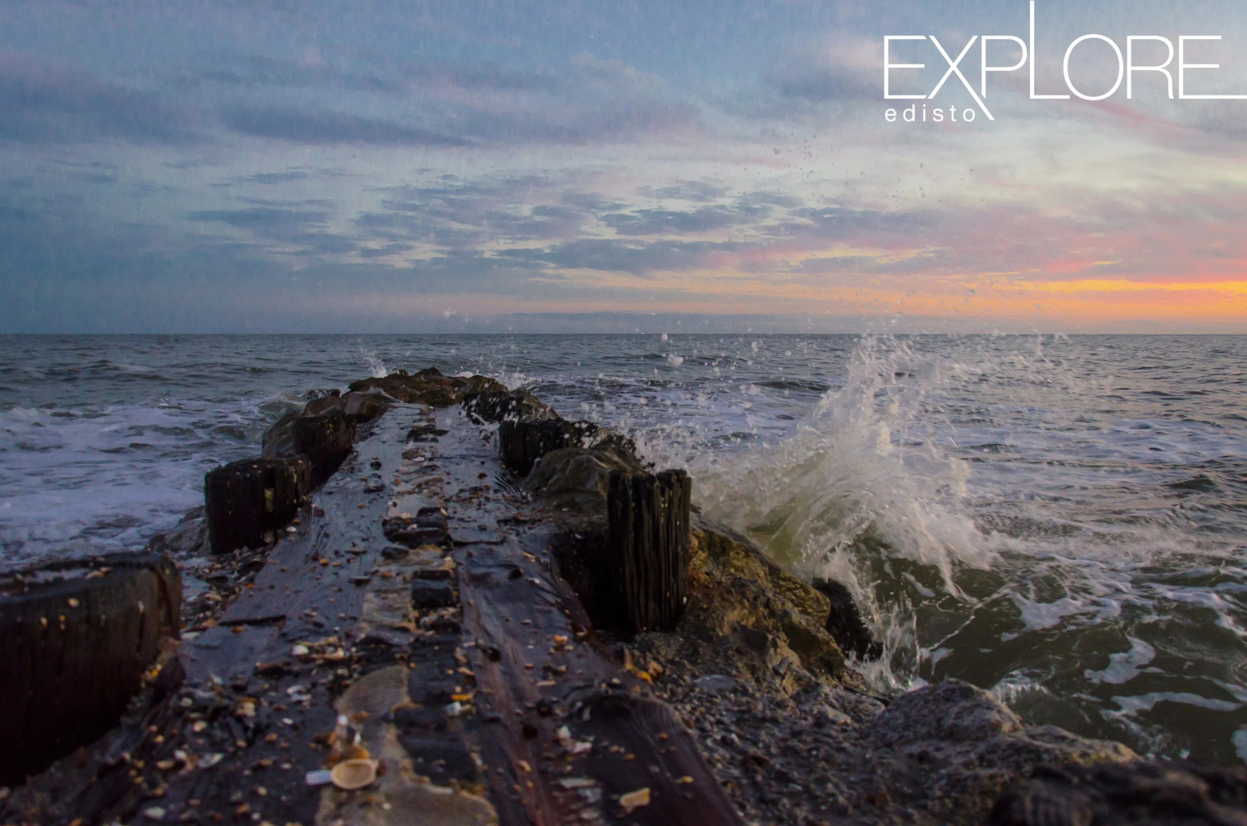 Pastel sky and wave crashing on a jetty.
