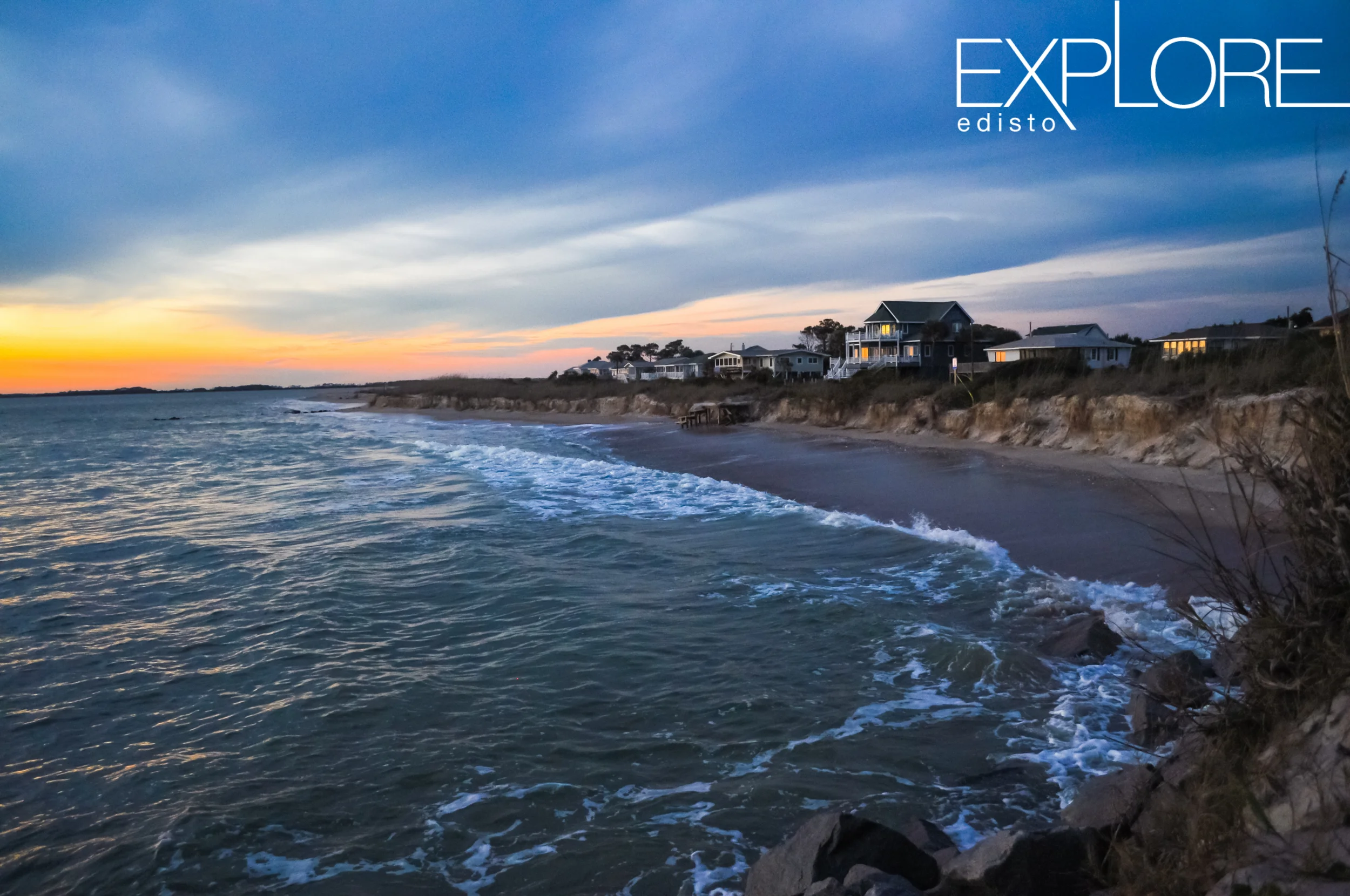 Light reflects from windows in beach houses in front of the ocean at sunset.
