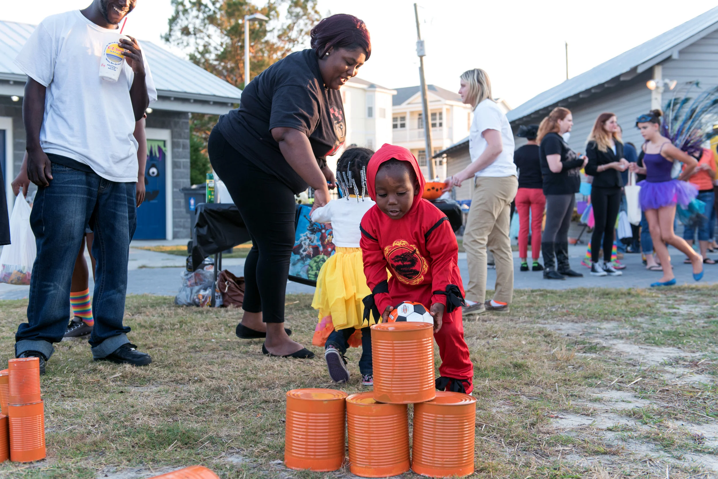 Young person tosses ball at pyramid of cans at Halloween Festival.