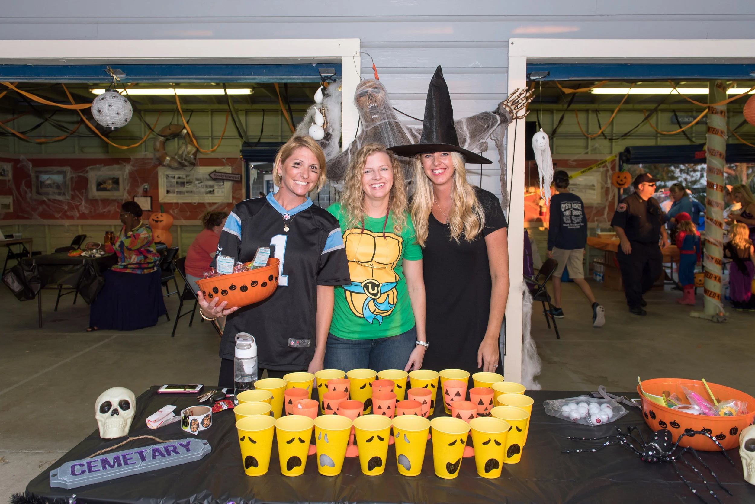 Three friends dressed as a football player, ninja turtle and witch pose in front of table at Halloween Festival.