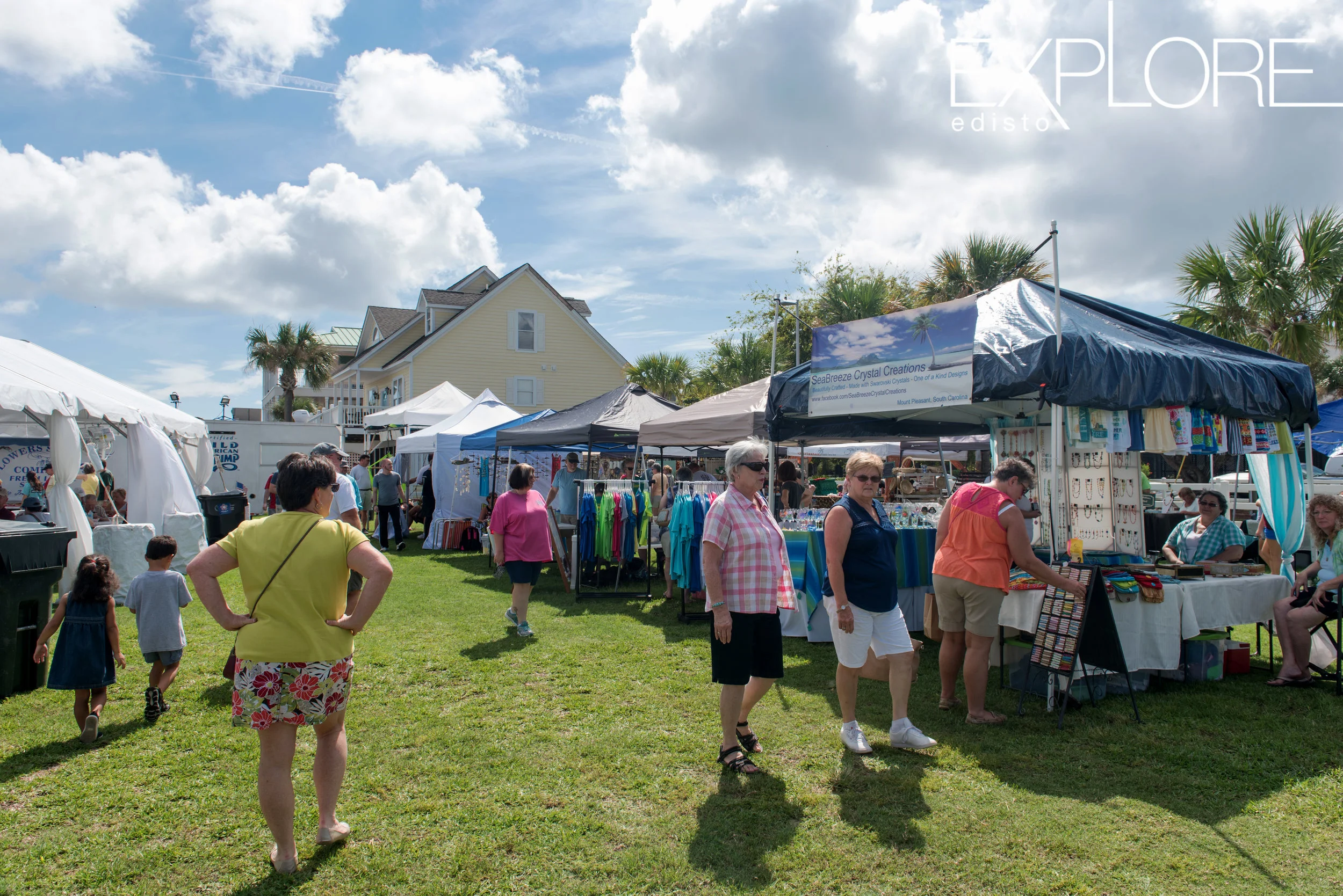 People mull about various vendors set up under tents on a bright but cloudy day.