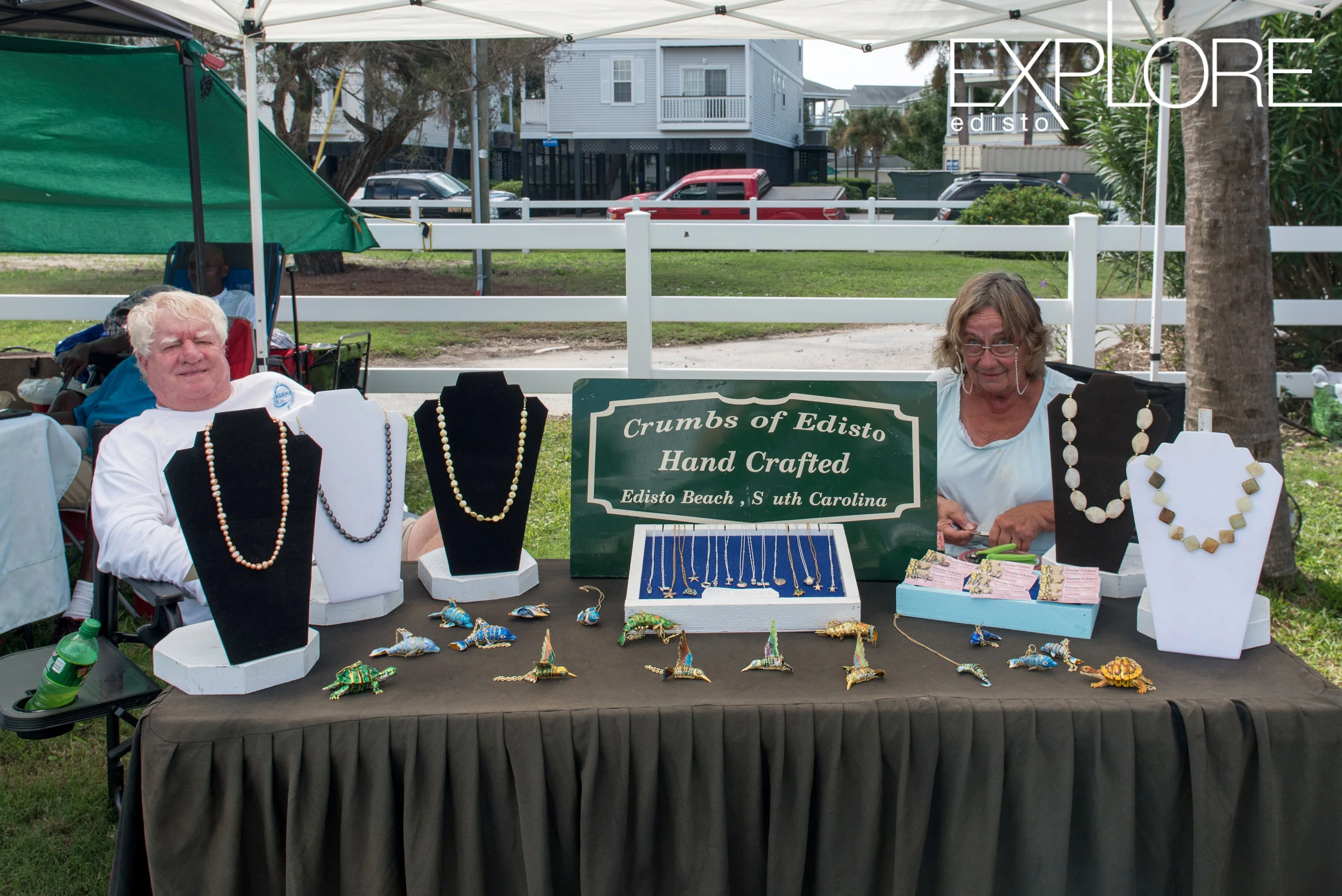 Man and women sit behind a table selling jewelry.