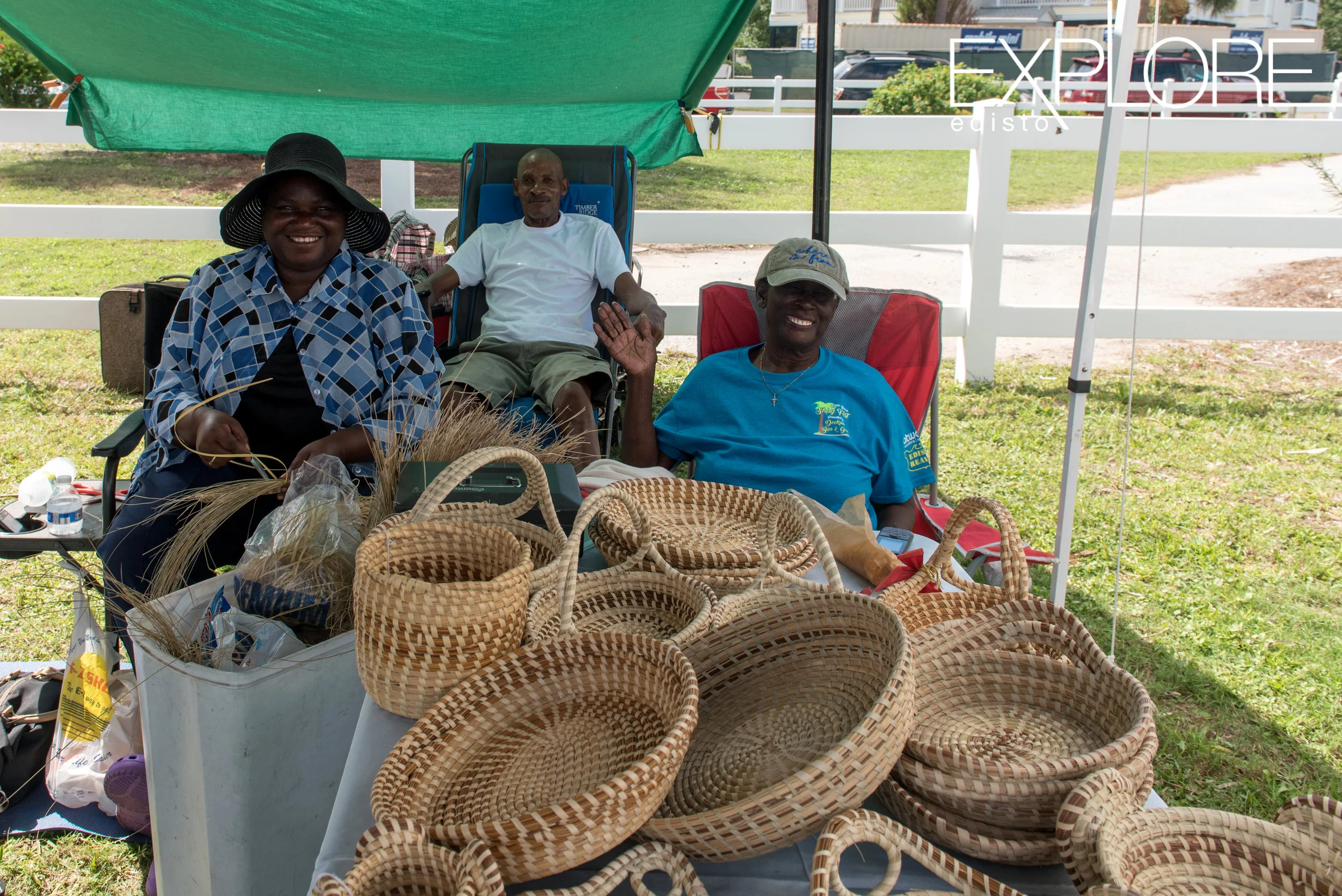 Two ladies and a gentleman behind a table of hand woven seagrass baskets.