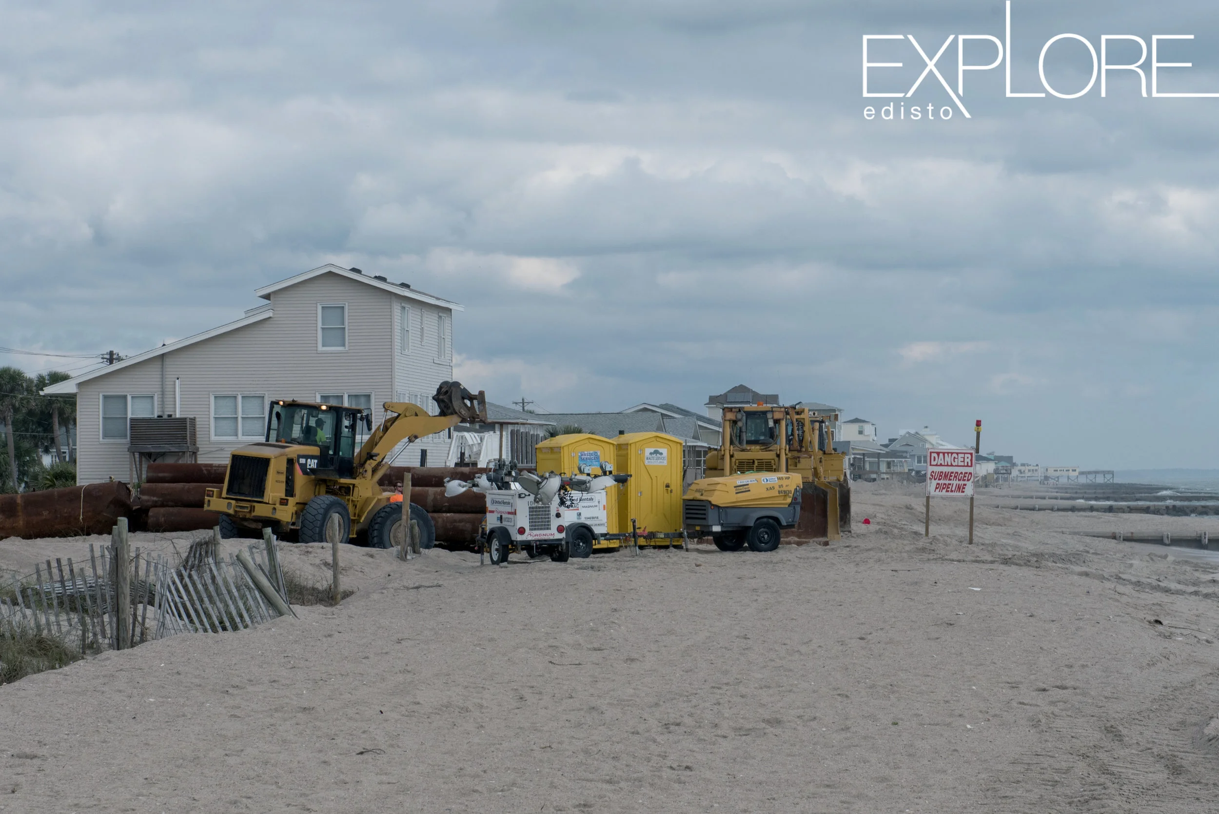 Portable toilets next to tractors on the beach.