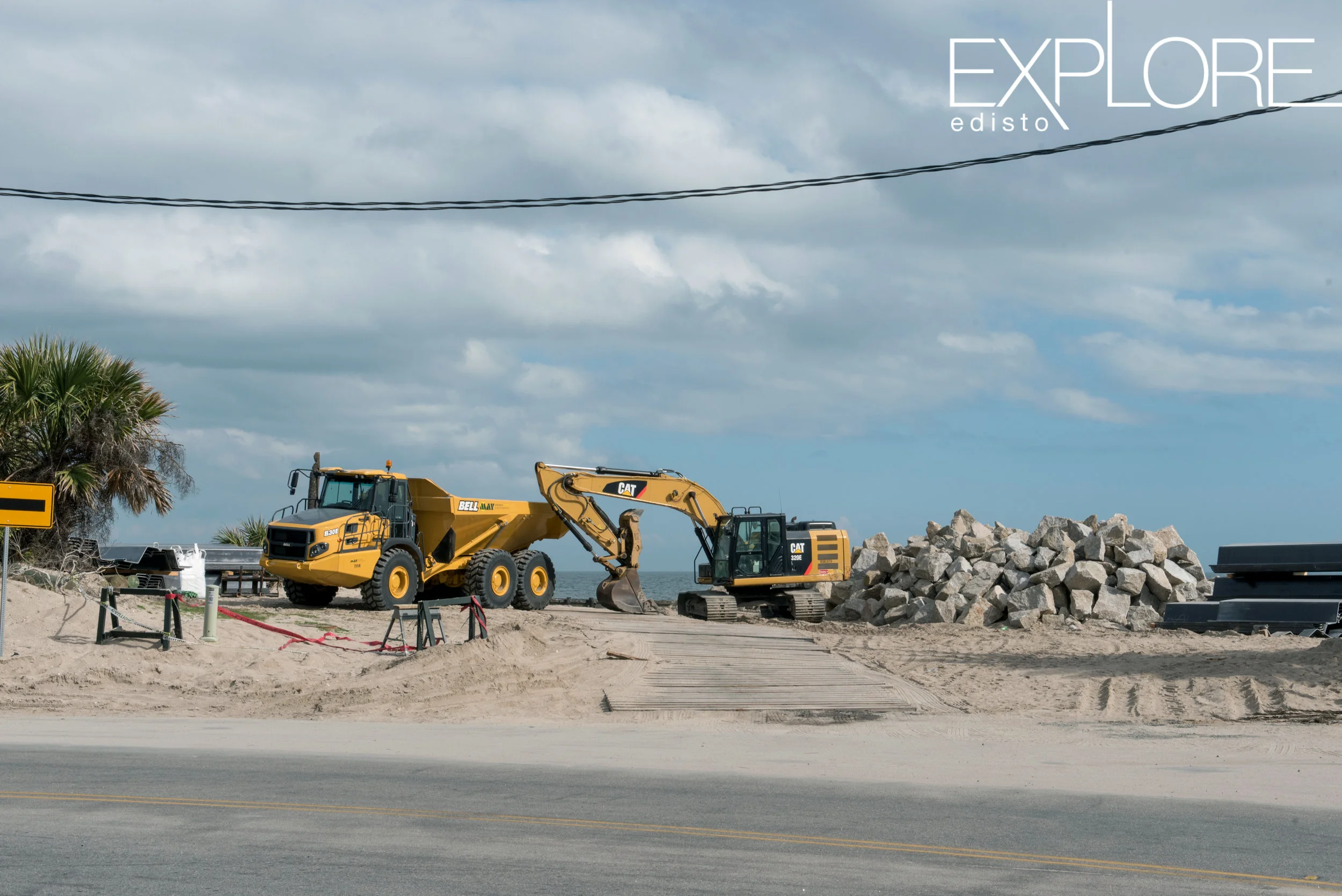 Tractors next to pile of rocks at the beach.
