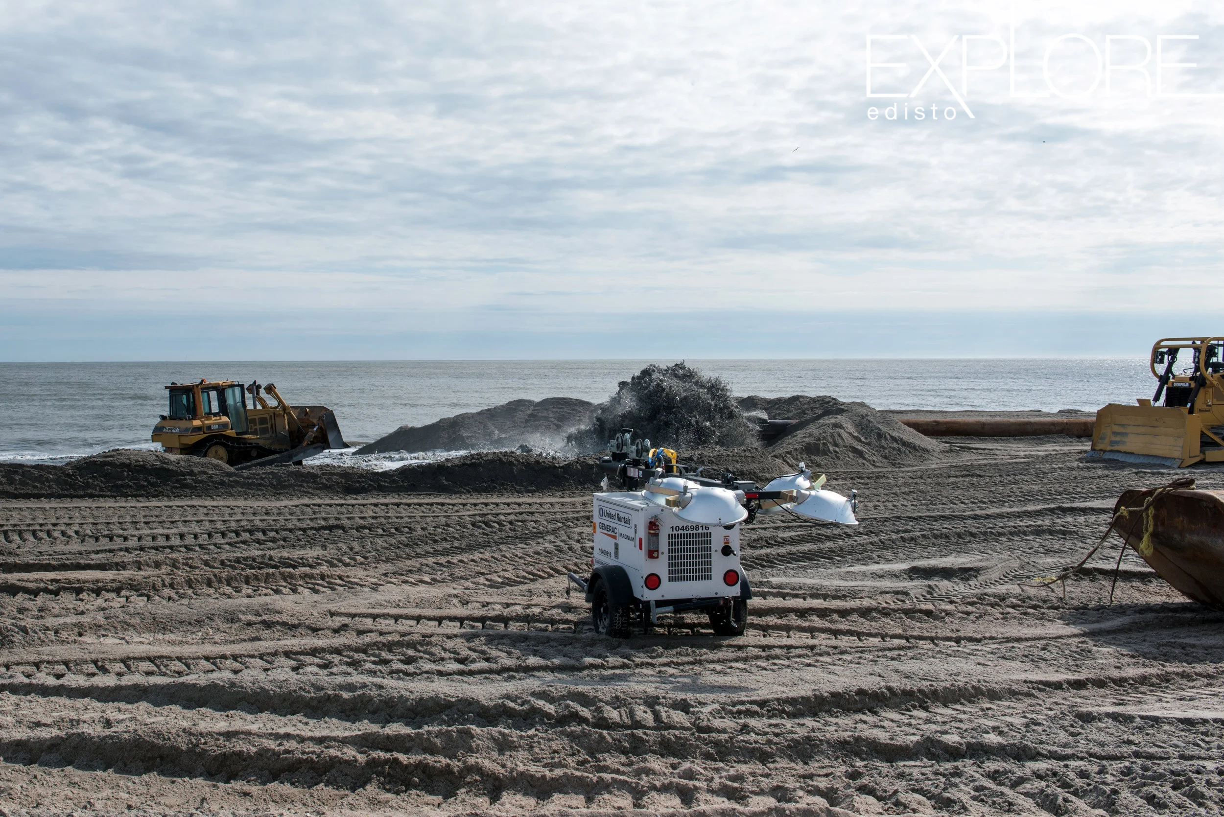 Tractors working and sand being pumped onto the beach from pipeline in ocean.