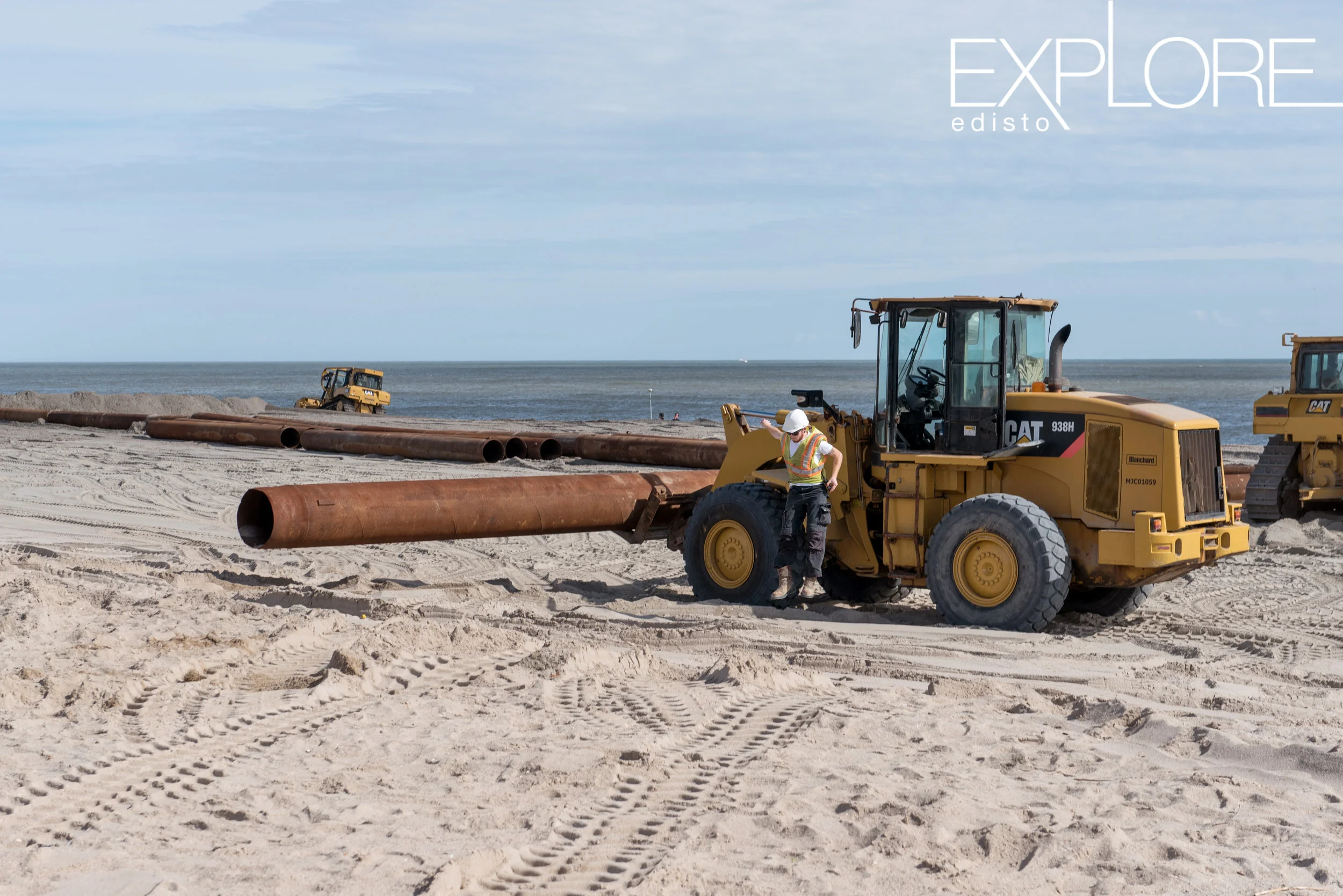 Man in hard hat jumps from tractor while working on the beach during beach renourishment.
