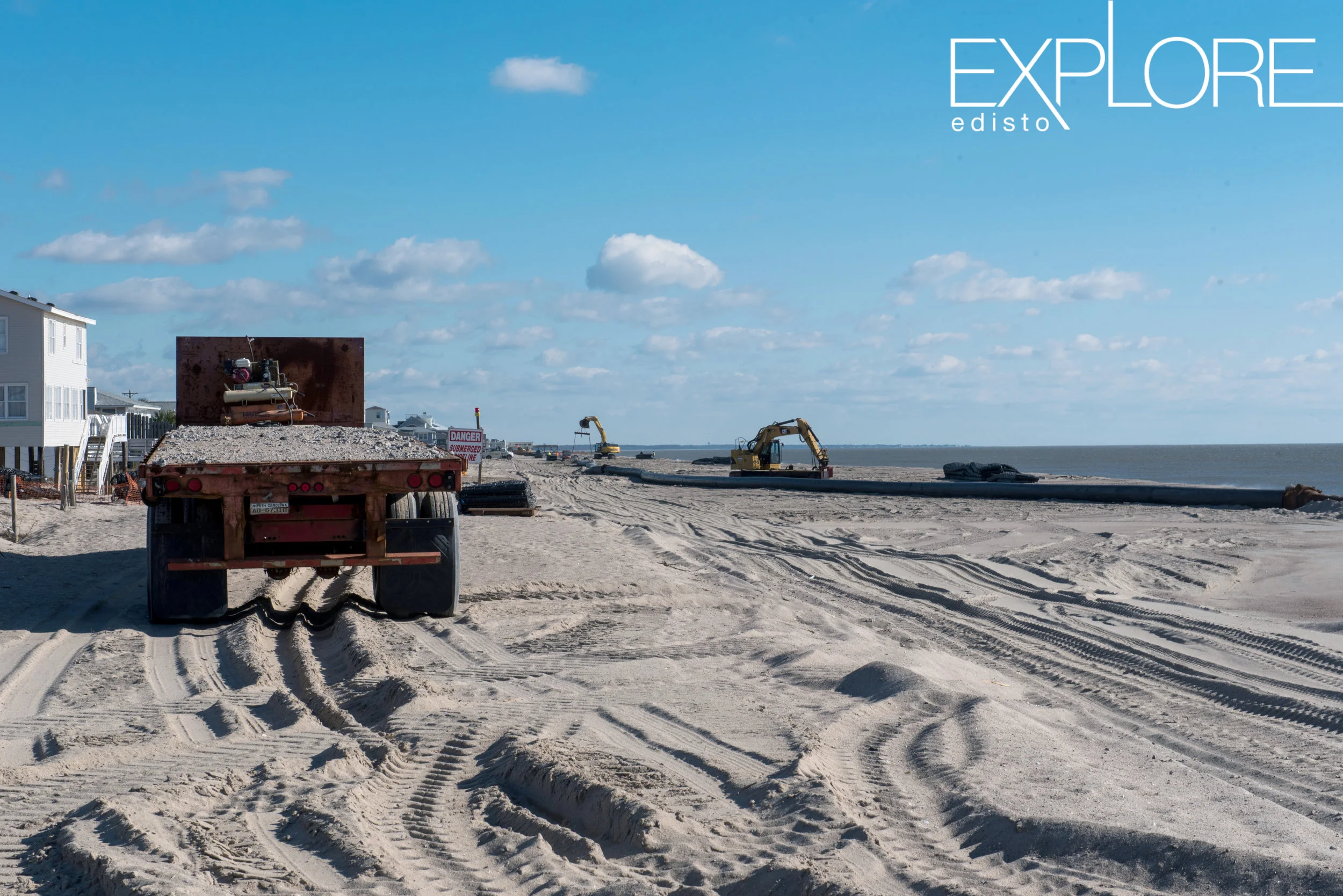 Flatbed truck on beach with tractors in the distance.