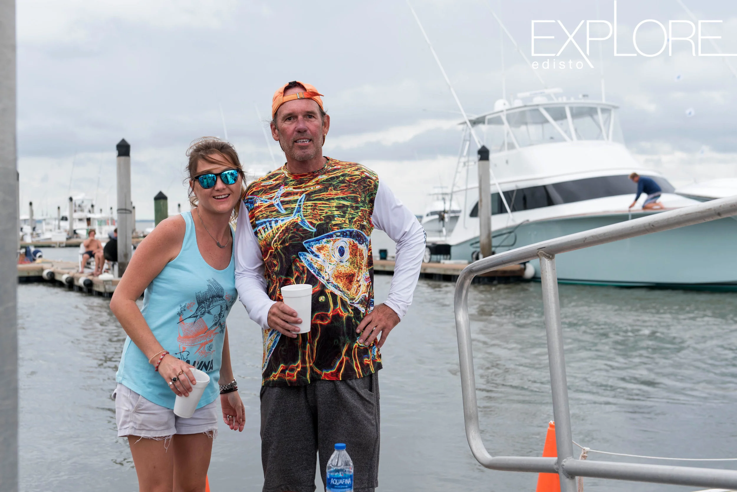 Husband and wife pose on dock in front of boats.