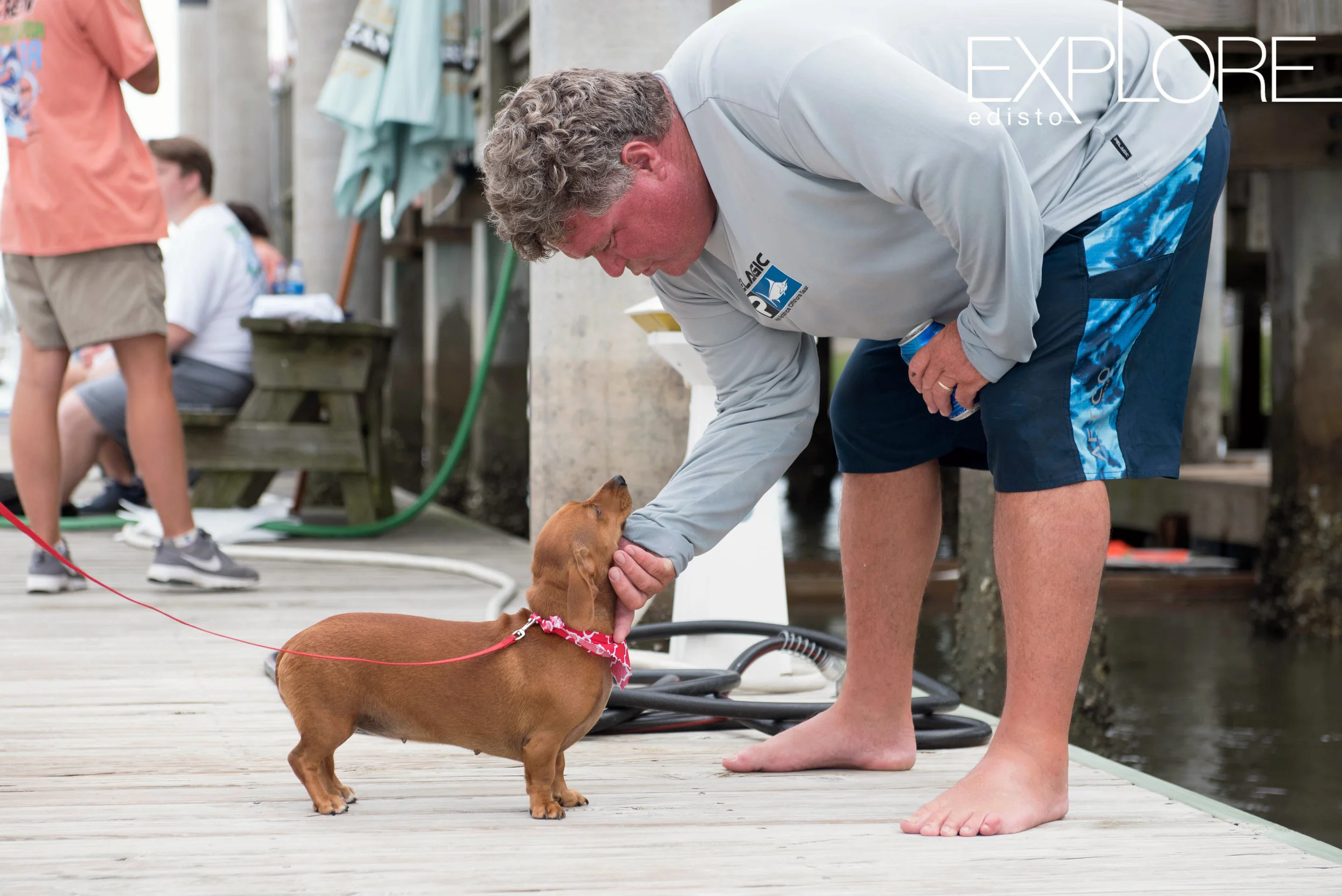 Man leans down to pet dachshund dog with red bandana.