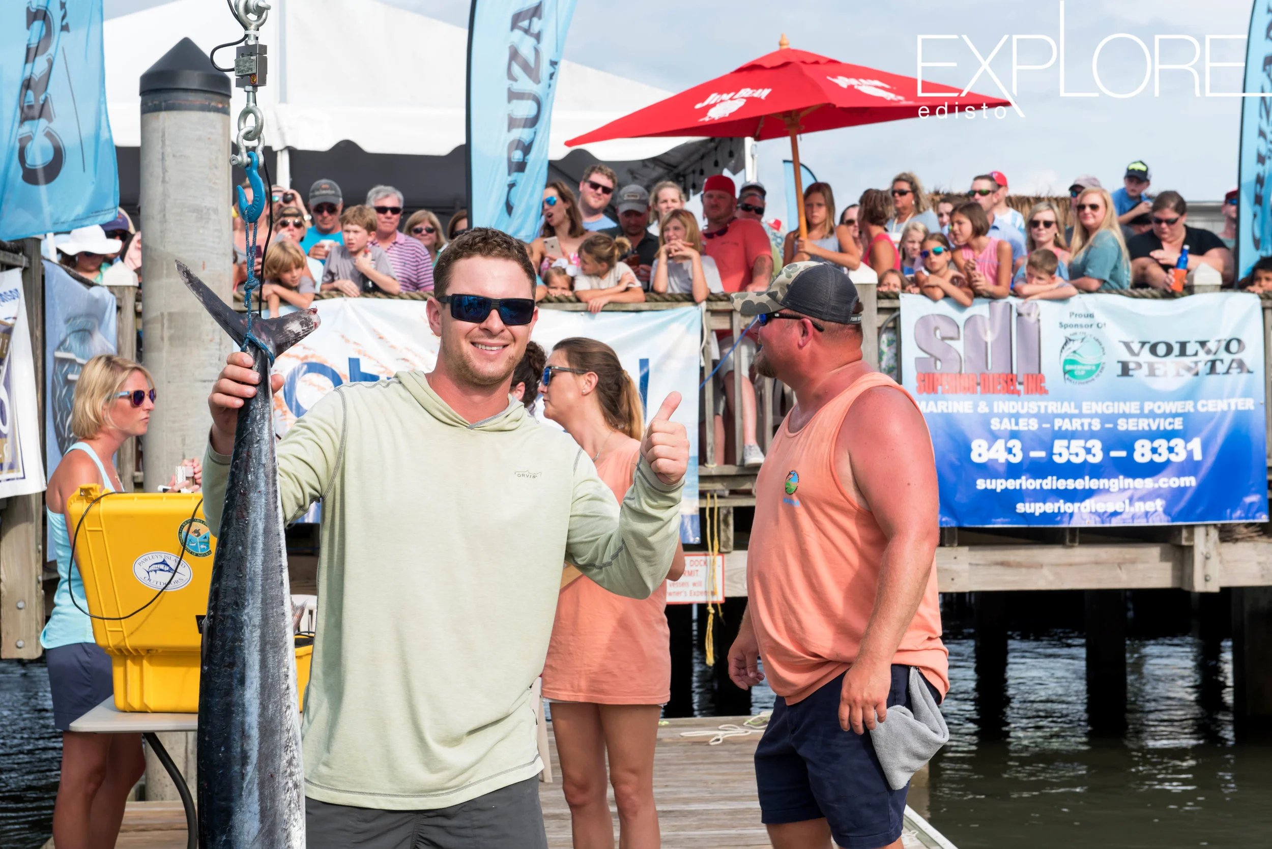 Guy in sunglasses gives a thumbs up while weighing-in fish.