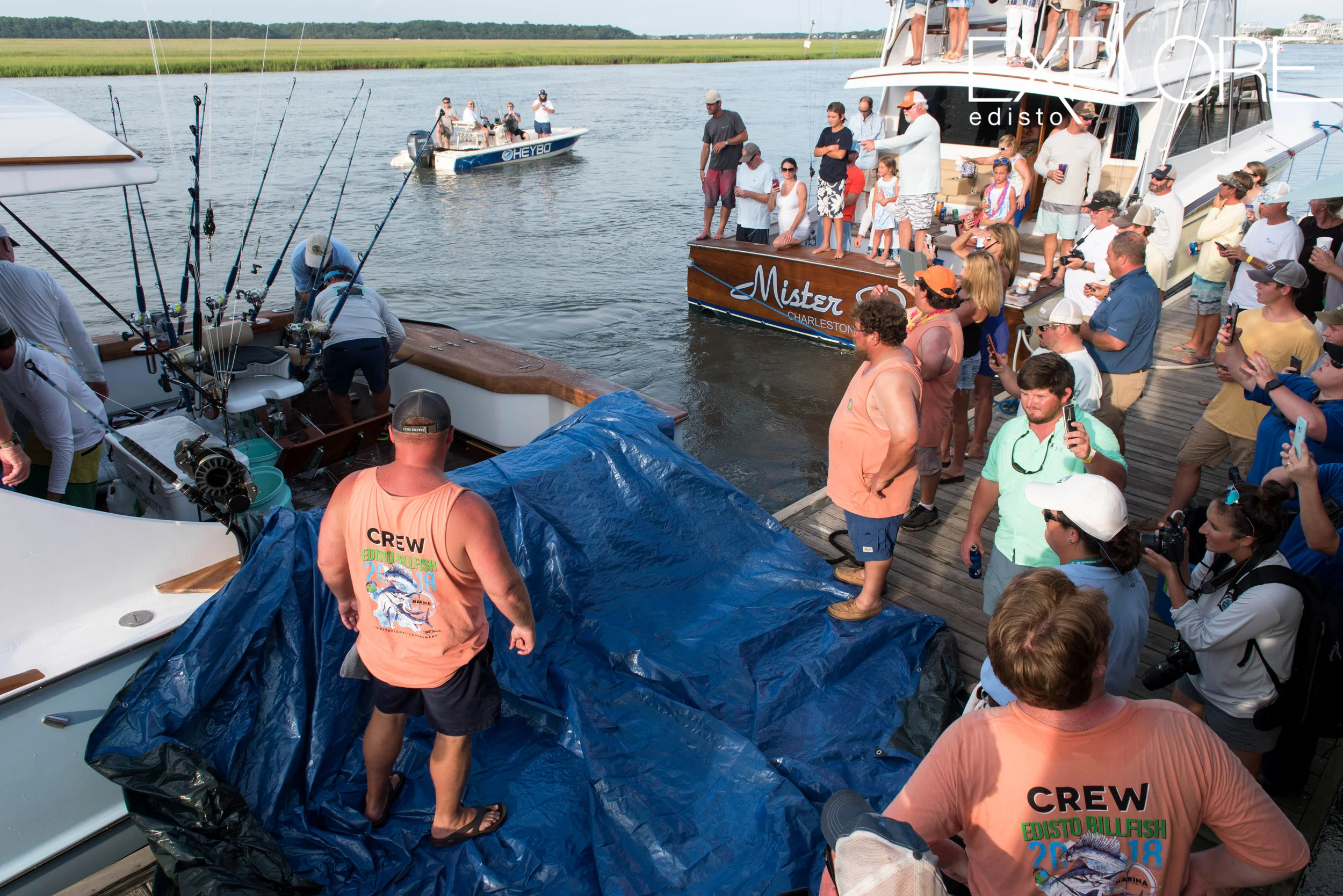 A blue tarp is laid out to assist in unloading the marlin. A crowd is gathered.