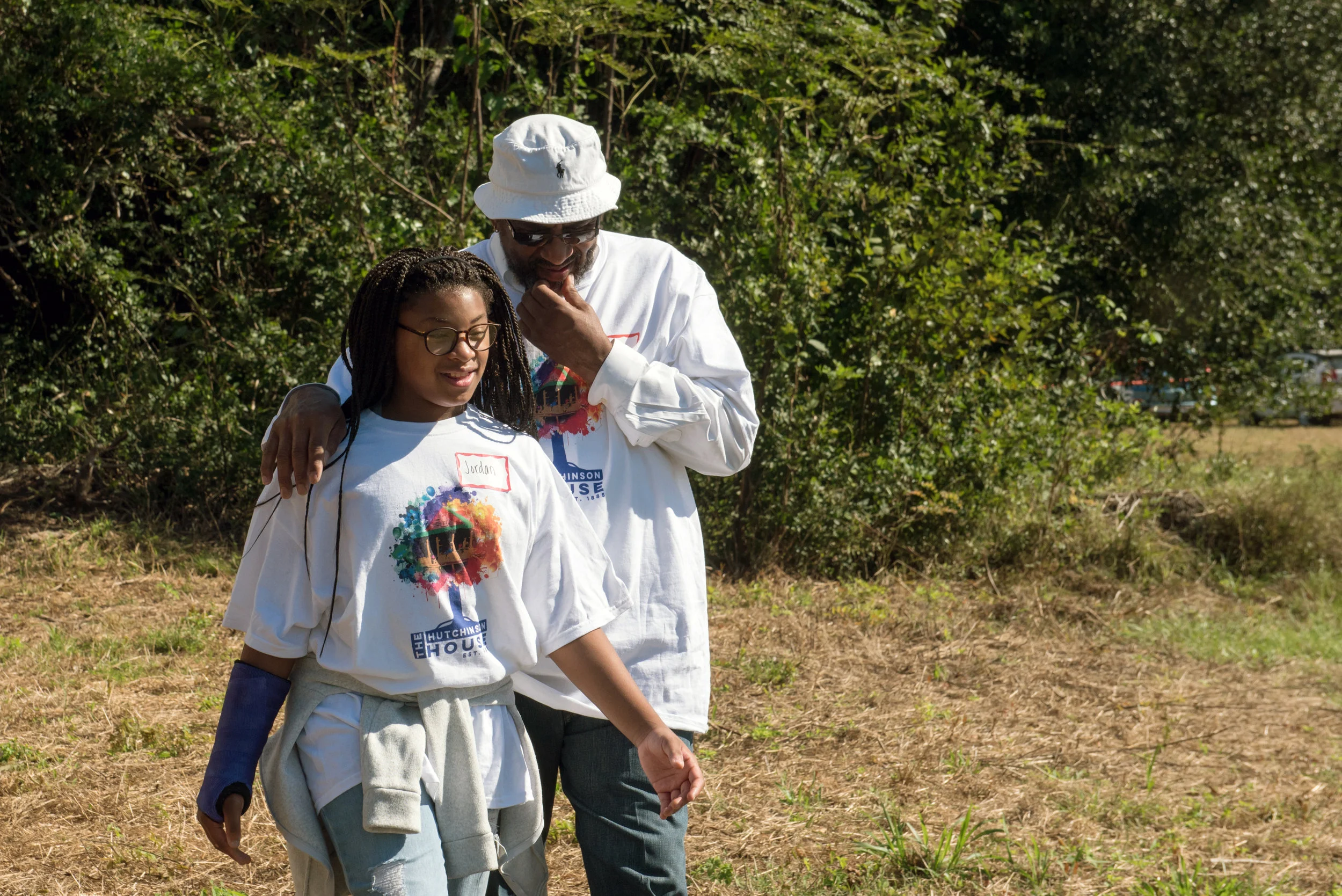 Man and girl walk through yard wearing Hutchinson House Family Reunion t-shirts.
