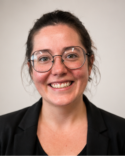 Smiling woman with glasses in a black blazer against a plain background.