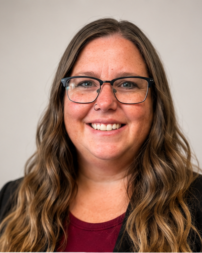 A smiling woman with long wavy brown hair, wearing glasses and a maroon top, against a neutral background.