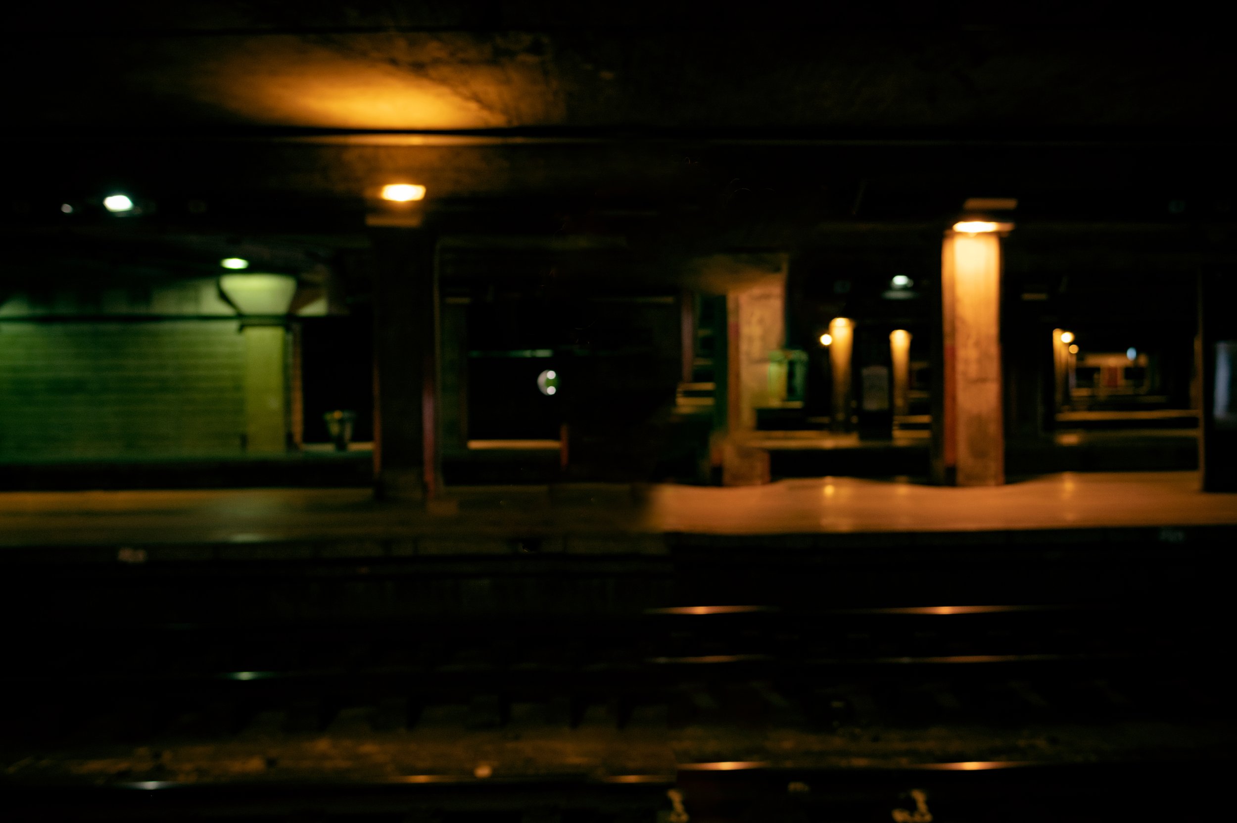 Nighttime view through a window showing a dark outdoor scene with dimly lit interior structures, illuminated by a few small lights and a faint glow in the sky.