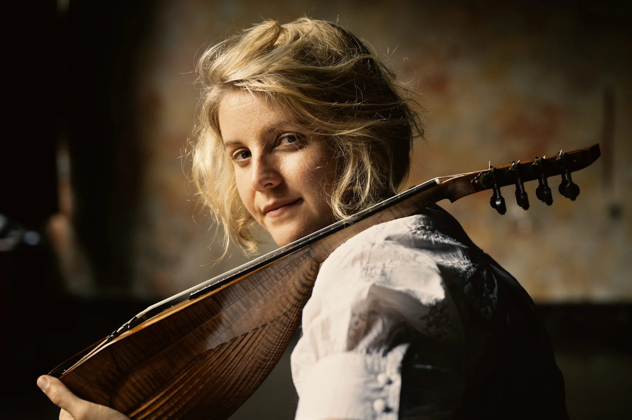 Woman with blonde hair playing a guitar looking over her shoulder