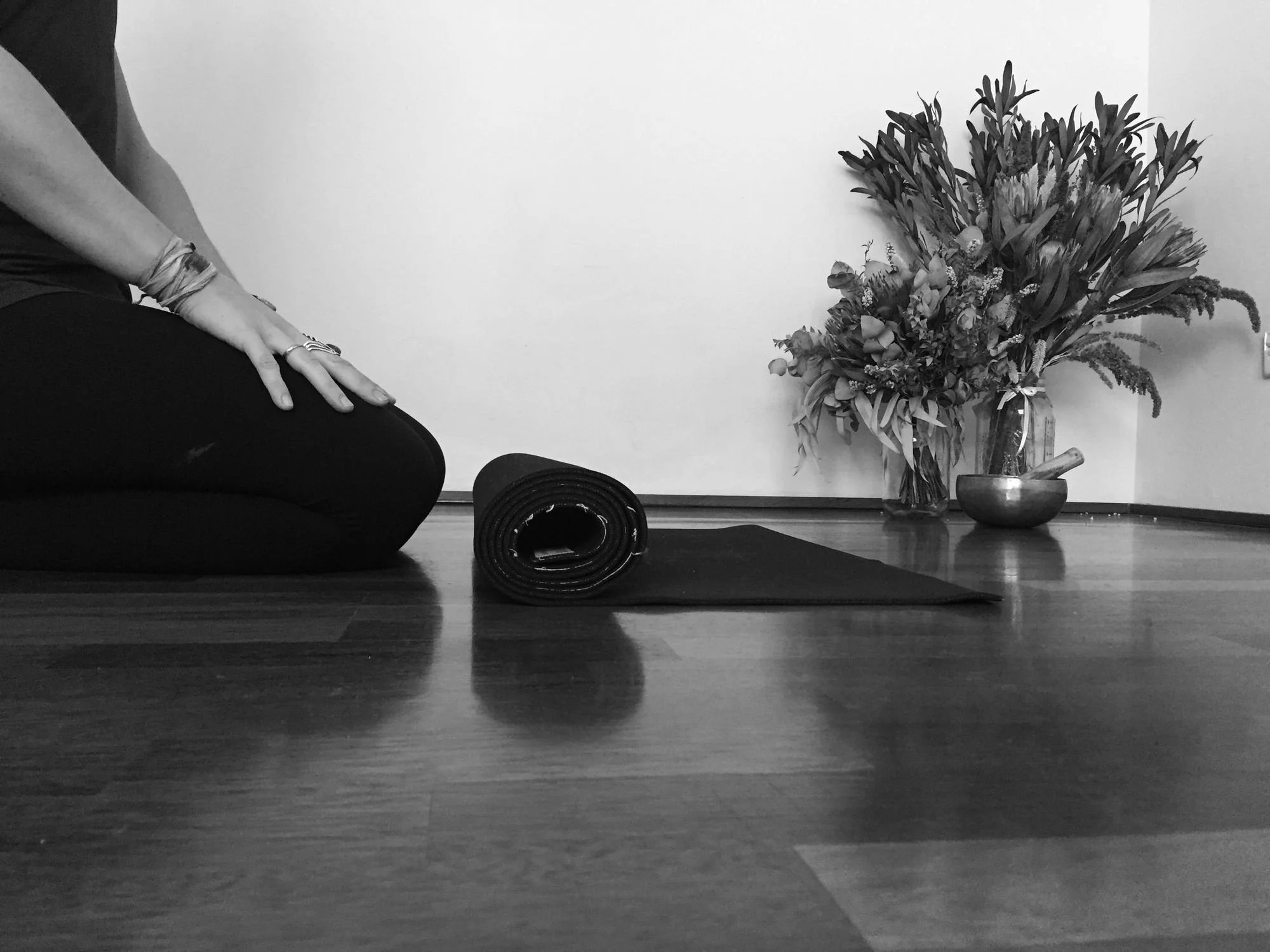 Corporate wellness: person kneeling beside a rolled-up yoga mat, with flowers and a singing bowl behind, black and white