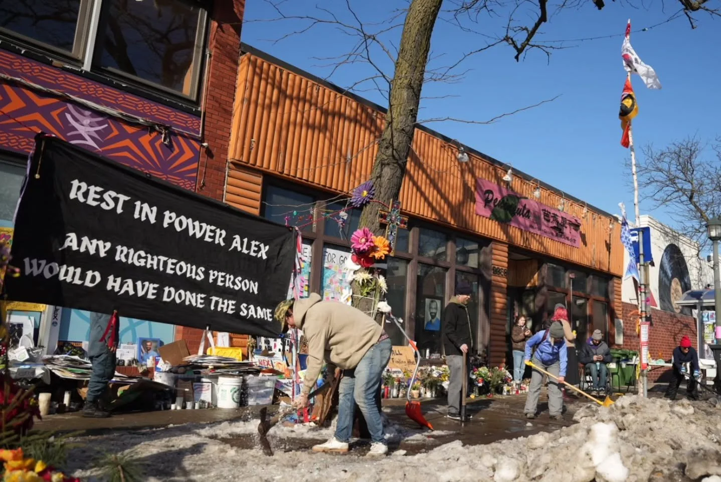 Yesterday, Feb 12, for the second day in a row, a group of volunteers showed up at Alex Pretti&rsquo;s memorial site, sorting and organizing signs, cleaning stuffed animals, clearing away old flowers, and pickaxing ice off the sidewalk, working tirel
