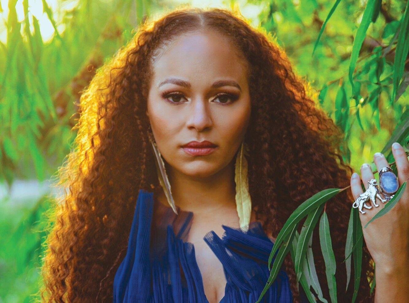 Photo of Robin Barnes with gold feather earings with a backdrop of weeping willow trees.