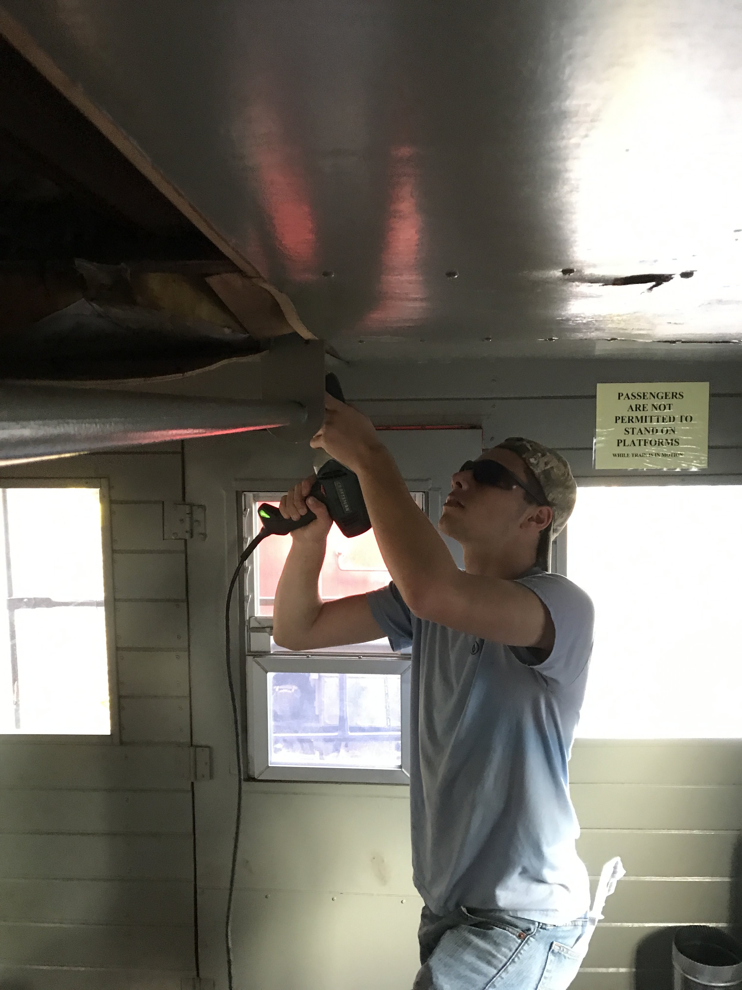  Matt Herman unscrewing wood panels which were used to replace the ceiling in part of the caboose which caught fire in the Conrail era. 