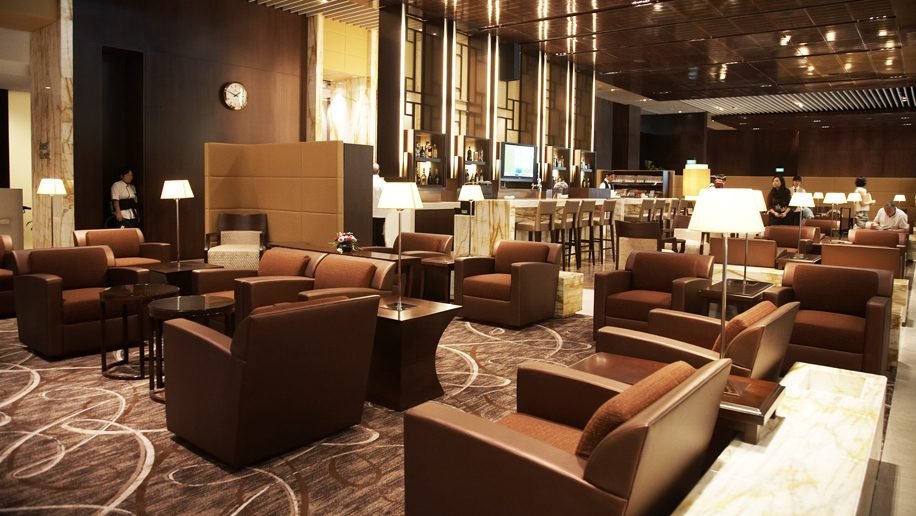 A huge Singapore Airlines airport loung. Vast brown carpeted space with brown leather armchairs, a bar, lamps, and gleaming decor.