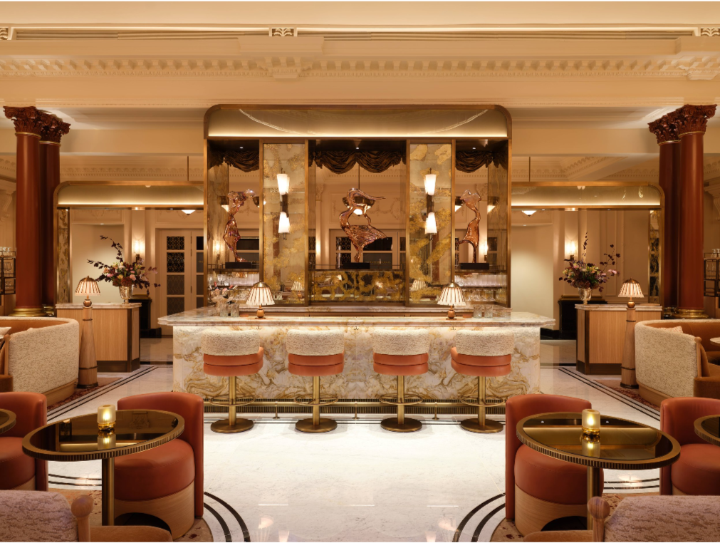 An opulent, luxury art deco bar in The Savoy Hotel, London.  With immaculate cream and orange stools, seats, private booths, candles on tables and a mirrored bar front and centre of it all.