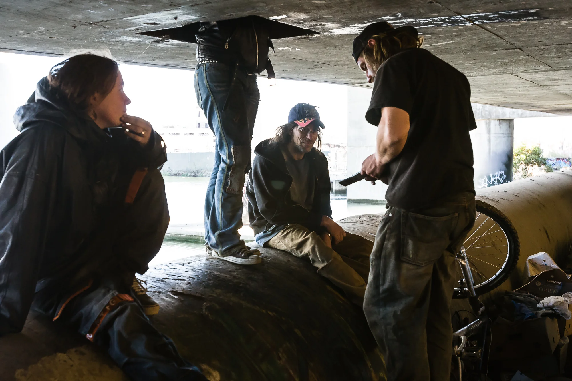 Homeless from neighboring camps gather at this camp after hearing word of a highly profitable scrap source. One scrapper calls his contact to verify the information.
