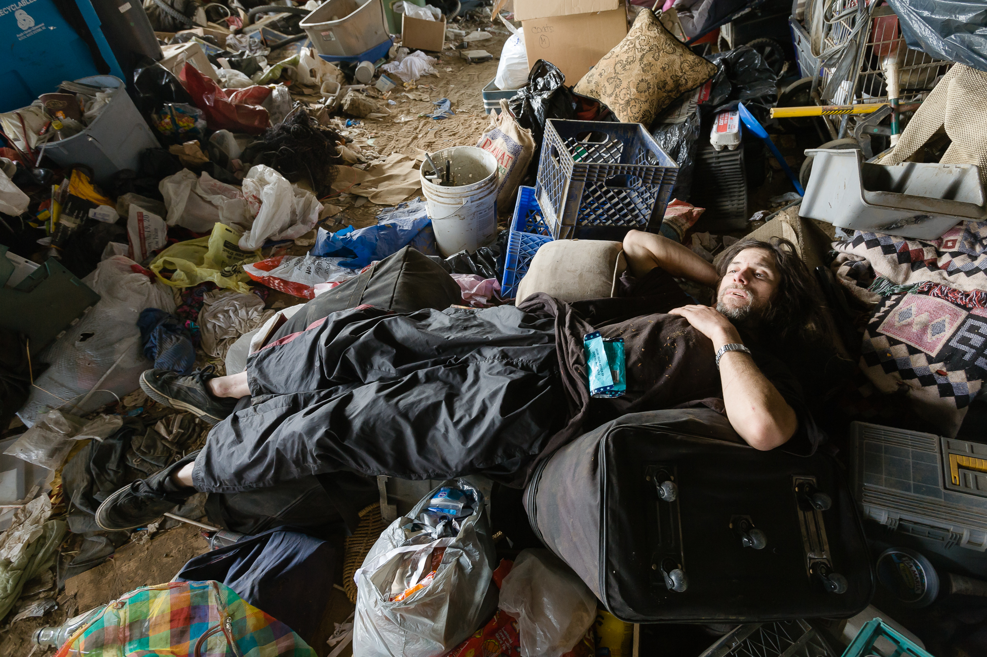 After a hard day of scrapping, Steve, lays down in a rat's nest of detritus back at camp to ponder his situation. New to the camp he lives in a make shift tent amongst a pile of garbage. 