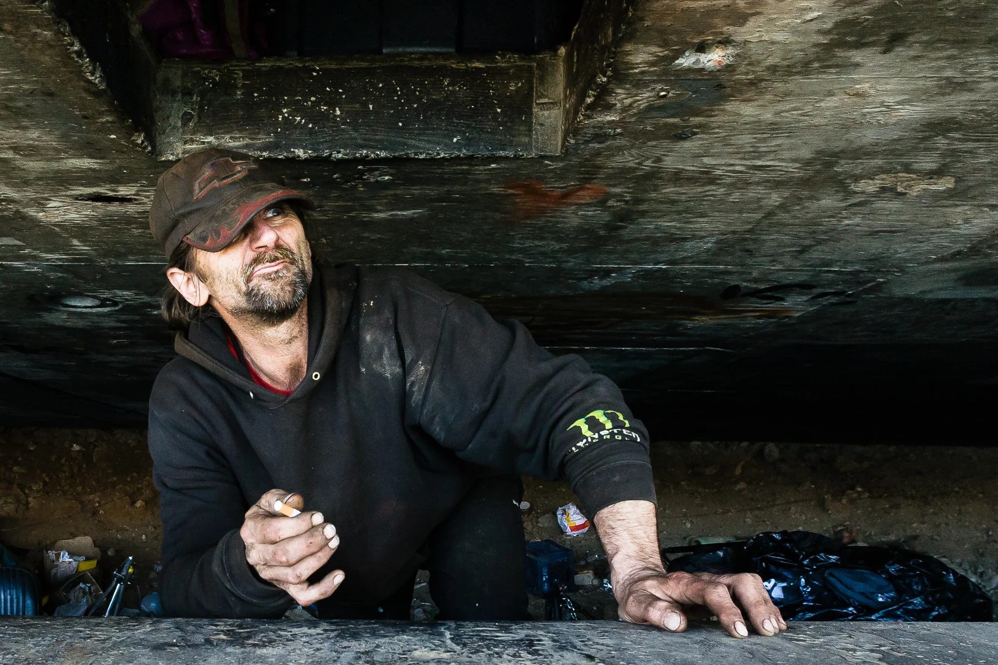 Sheriff's deputies have been raiding the camp recently looking for parol dodgers. Steve, a veteran scrapper and long time resident of the camp, waits ready to barricade himself in his hole as he watches a patrol car park near the encampment.