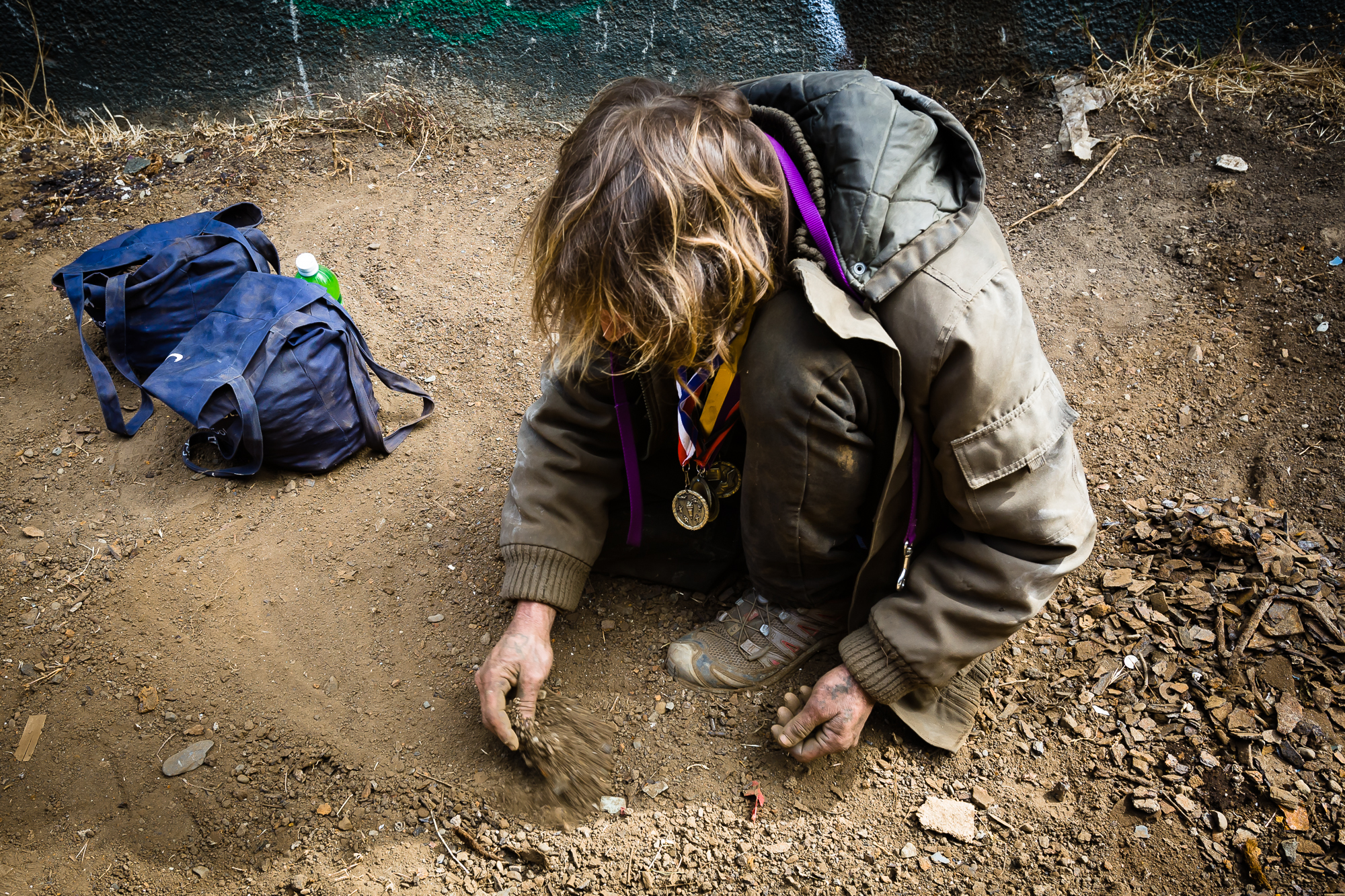  While waiting for his partners to show-up to an abandoned factory, Mike sifts through the dirt outside of the building entrance looking for scraps of non-ferrous metal. There is over 100lbs of metal chips in the two blue bags, and another pile growi