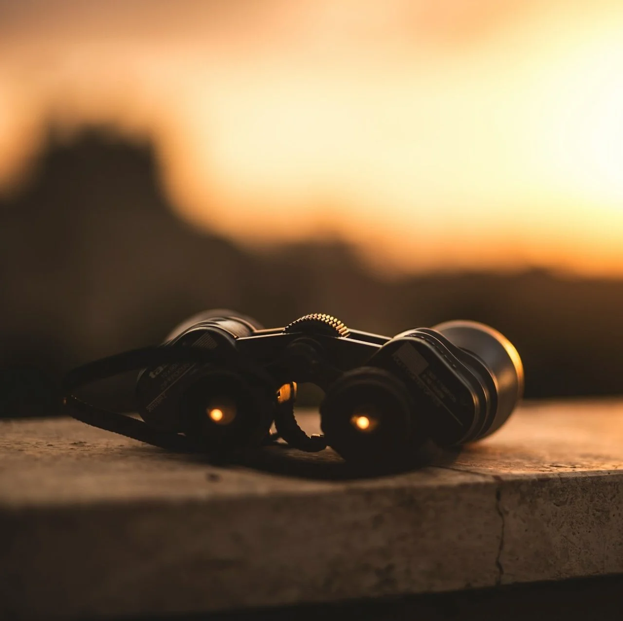 Binoculars resting on a ledge overlooking a sunset