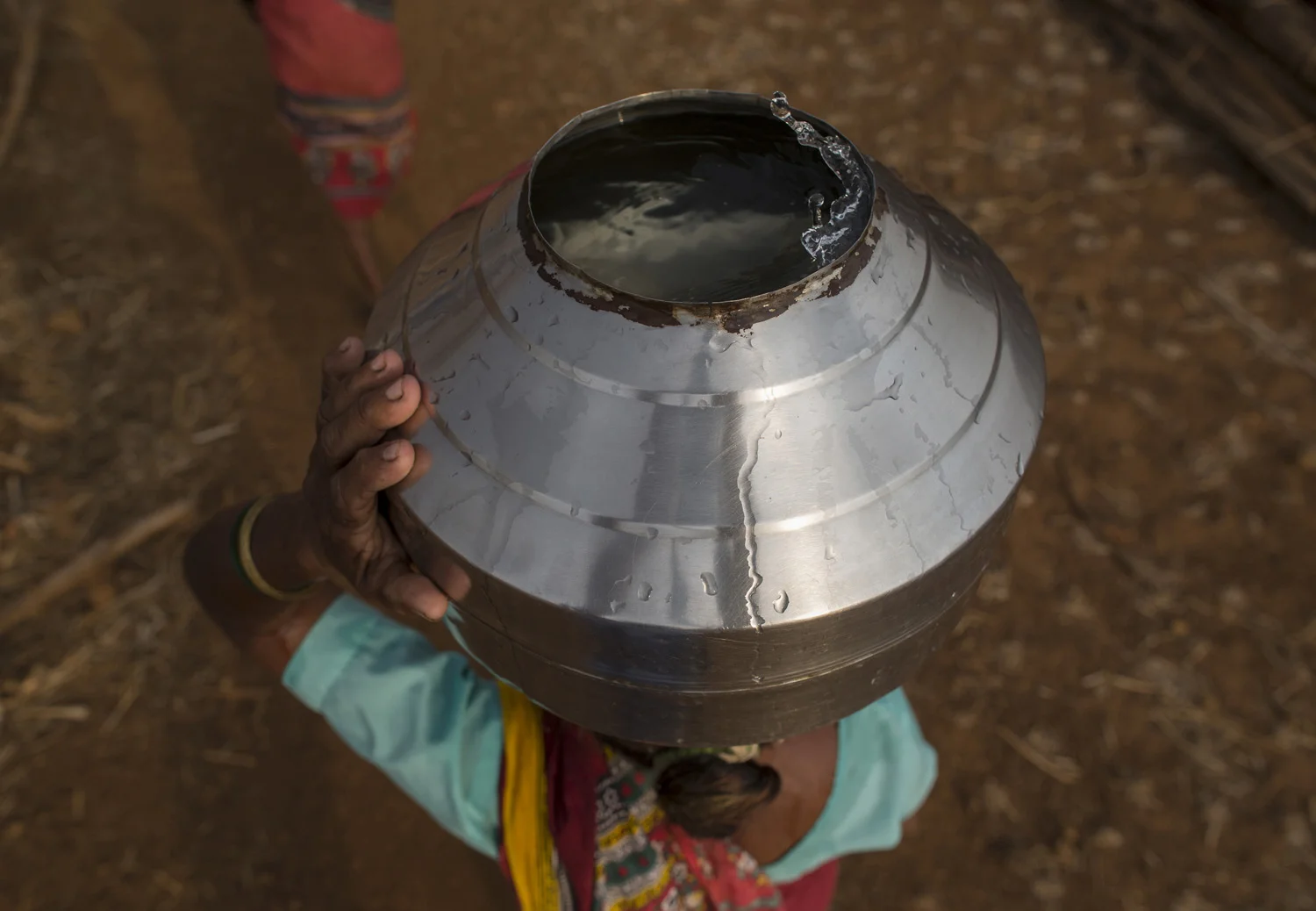 Bhaagi, third wife of Sakharam Bhagat, carries a metal pitcher filled with water from a well outside Denganmal village.