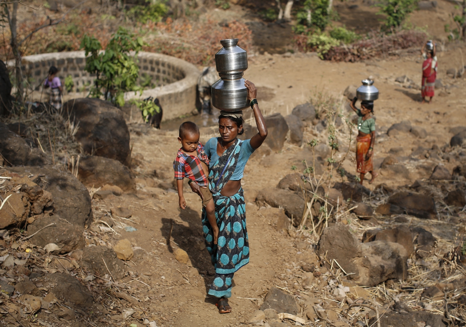  Shivarti, second wife of Namdeo, carries her grandson while carrying metal pitchers filled with water from a well outside Denganmal village. 