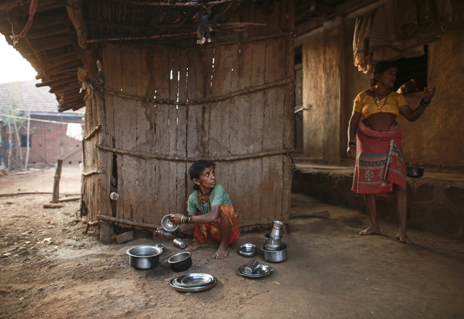  Sakhri (L), the second wife of Sakharam Bhagat, listens to Tuki, the first wife of Sakharam Bhagat as she washes utensils outside their house in Denganmal village. 