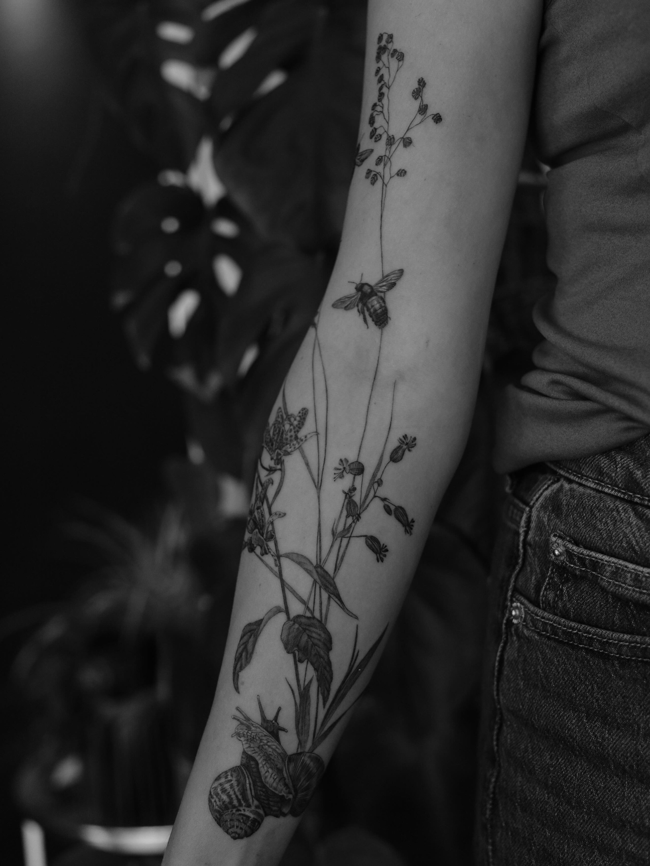 A little black &amp; grey fineline piece with a snail, carpenter bees and trembling grass 🖤
I made this custom botanical tattoo for someone who&rsquo;s actually allergic to bees and grass - which somehow made the whole idea even more special to tatt