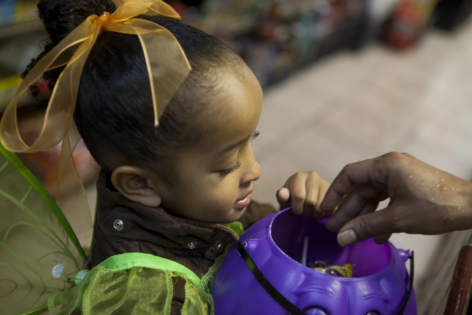 A clerk drops candy into her purple pumpkin head bucket.