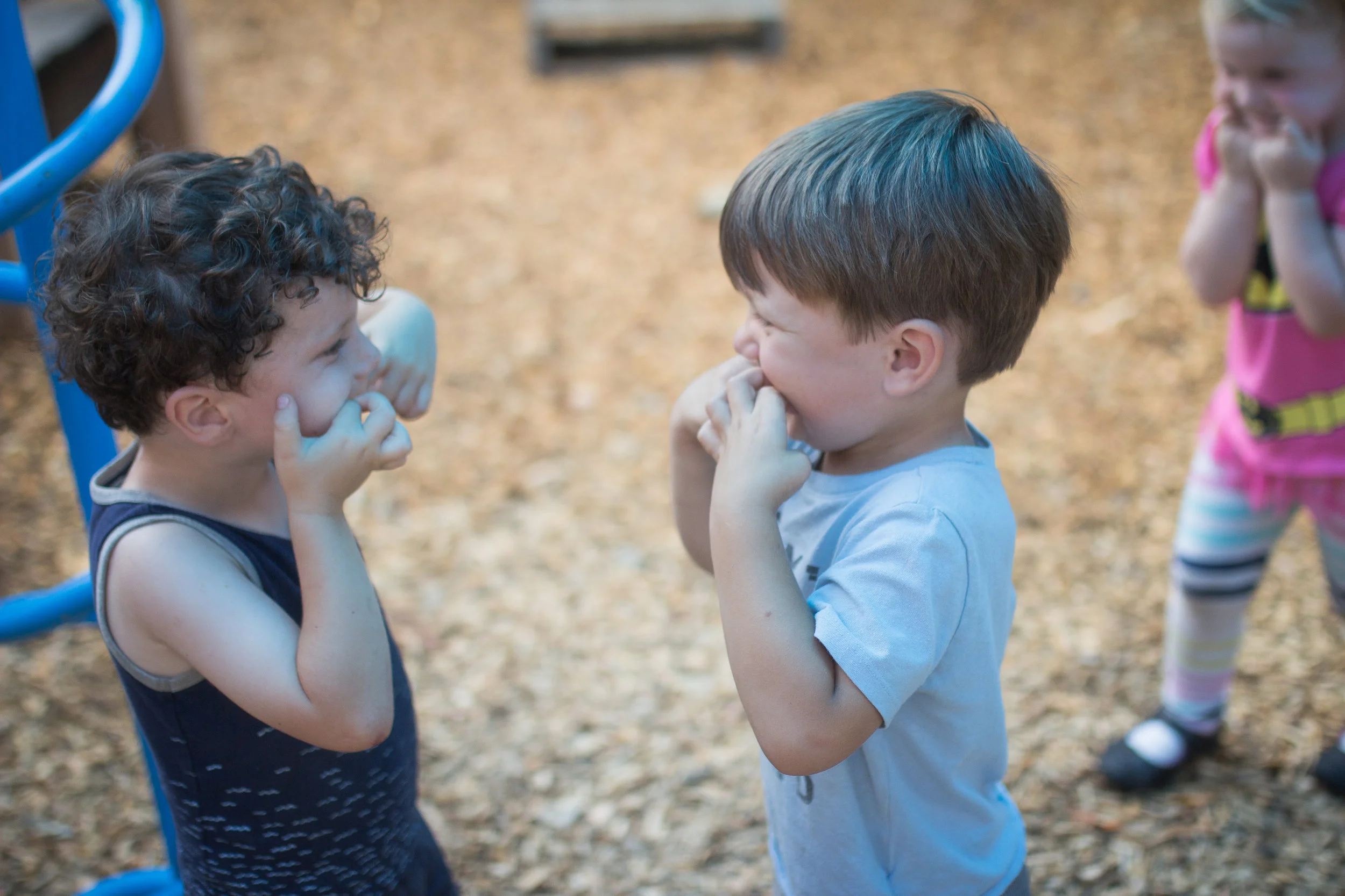 Three preschoolers connect by showing each other their funniest faces.
