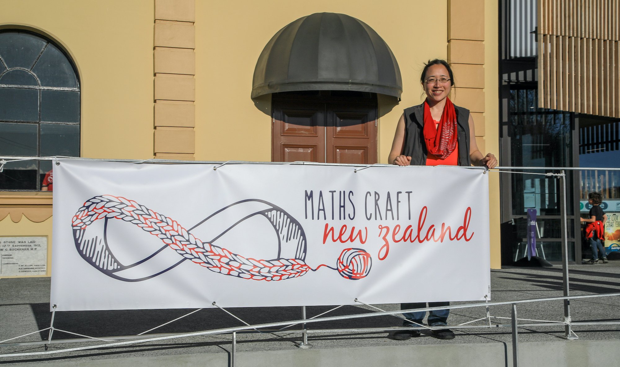 Eugenia Cheng standing behind the Maths Craft banner outside the Martinborough Town Hall