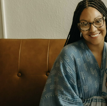Sadie Keegan sits on a brown couch with a blue shirt.  Her hair is in braids.